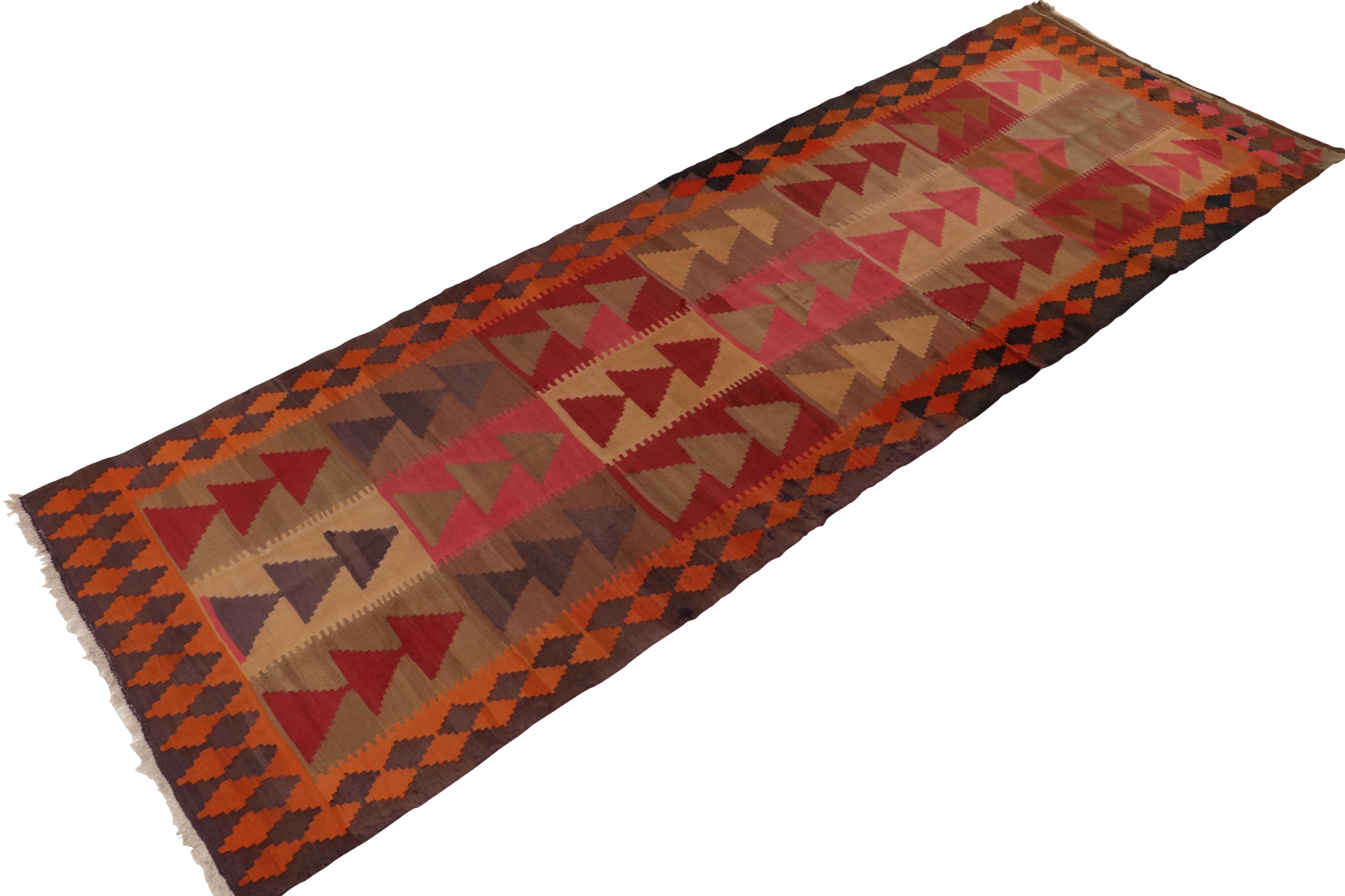 A vintage 4x13 Kilim rug, handwoven in wool originating from Turkey circa 1950-1960. Enjoying a play of the most unusual colors, primarily beige-brown with a unique gray-purple element alongside the red, pink, and orange lending a beautiful