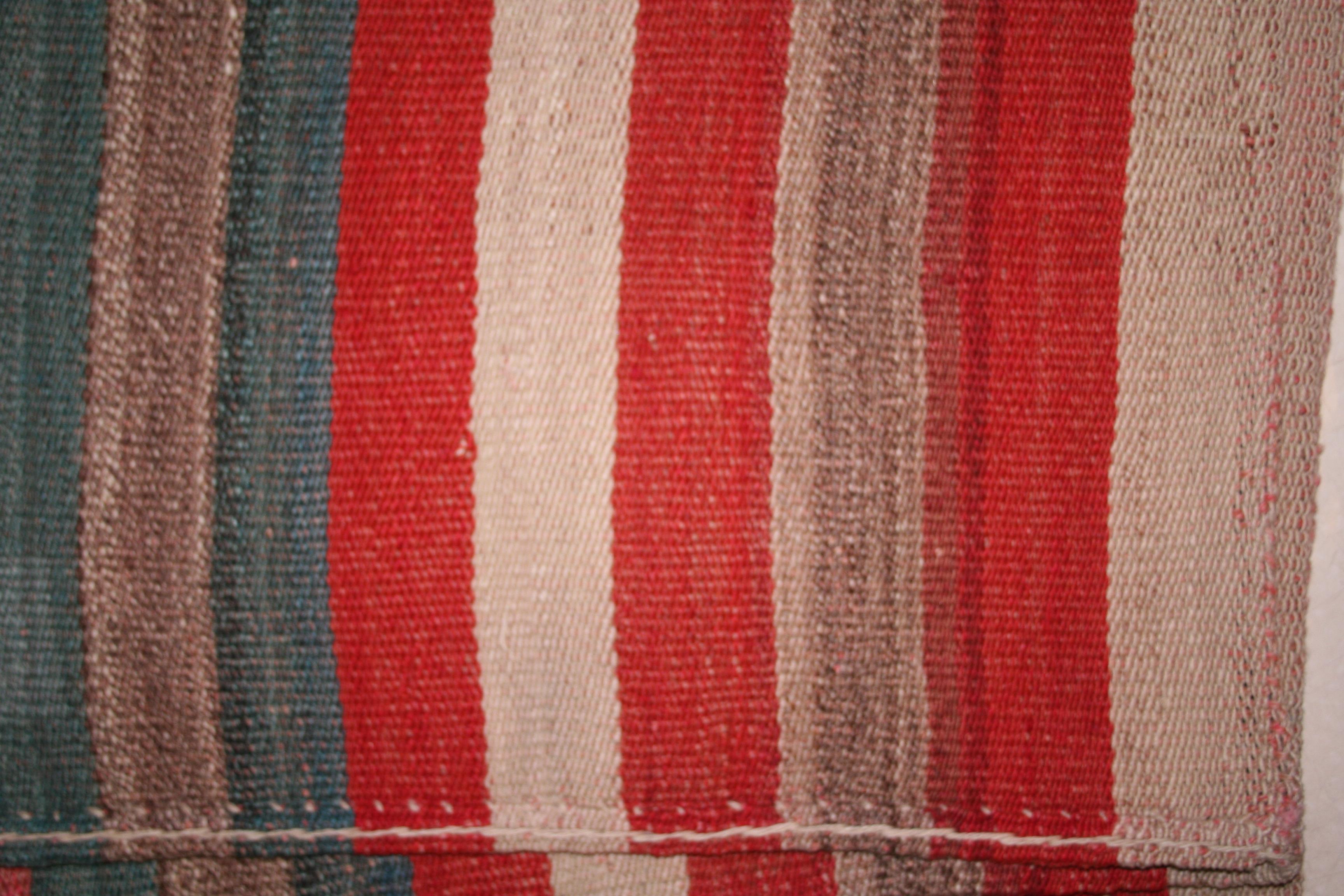 A very graphic tribal Kilim composed of two joined panels each containing an array of polychrome vertical stripes of various widths. The result is a wool flat-weave with a mirror image pattern having a central stripe that is considerably wider than