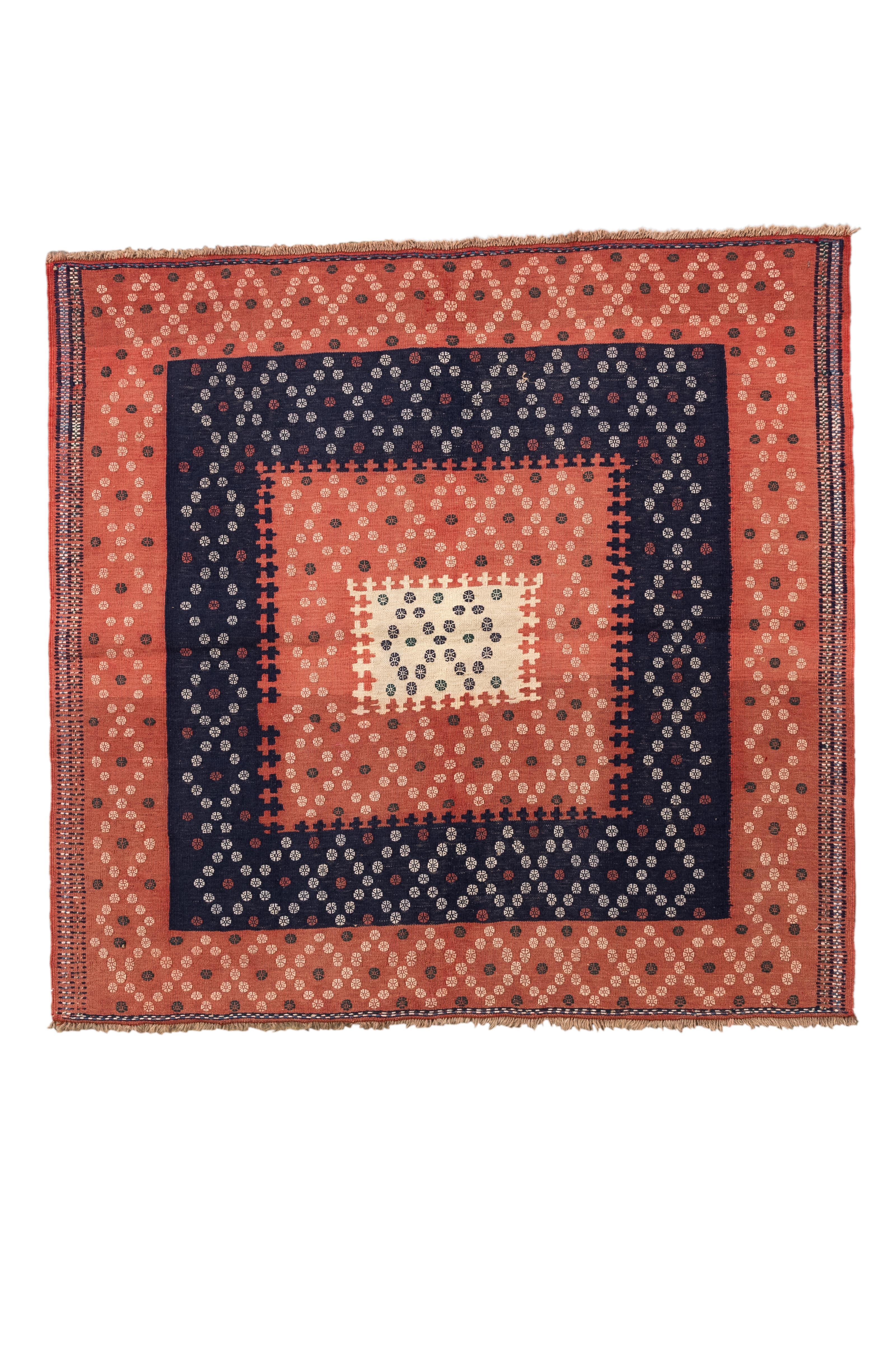 Questo Kilim tribale vintage presenta un sorprendente disegno concentrico composto da motivi a rombi e a punti. La disposizione è incentrata su un quadrato color crema e indaco, che si espande verso l'esterno in campi alternati di rosso terracotta e