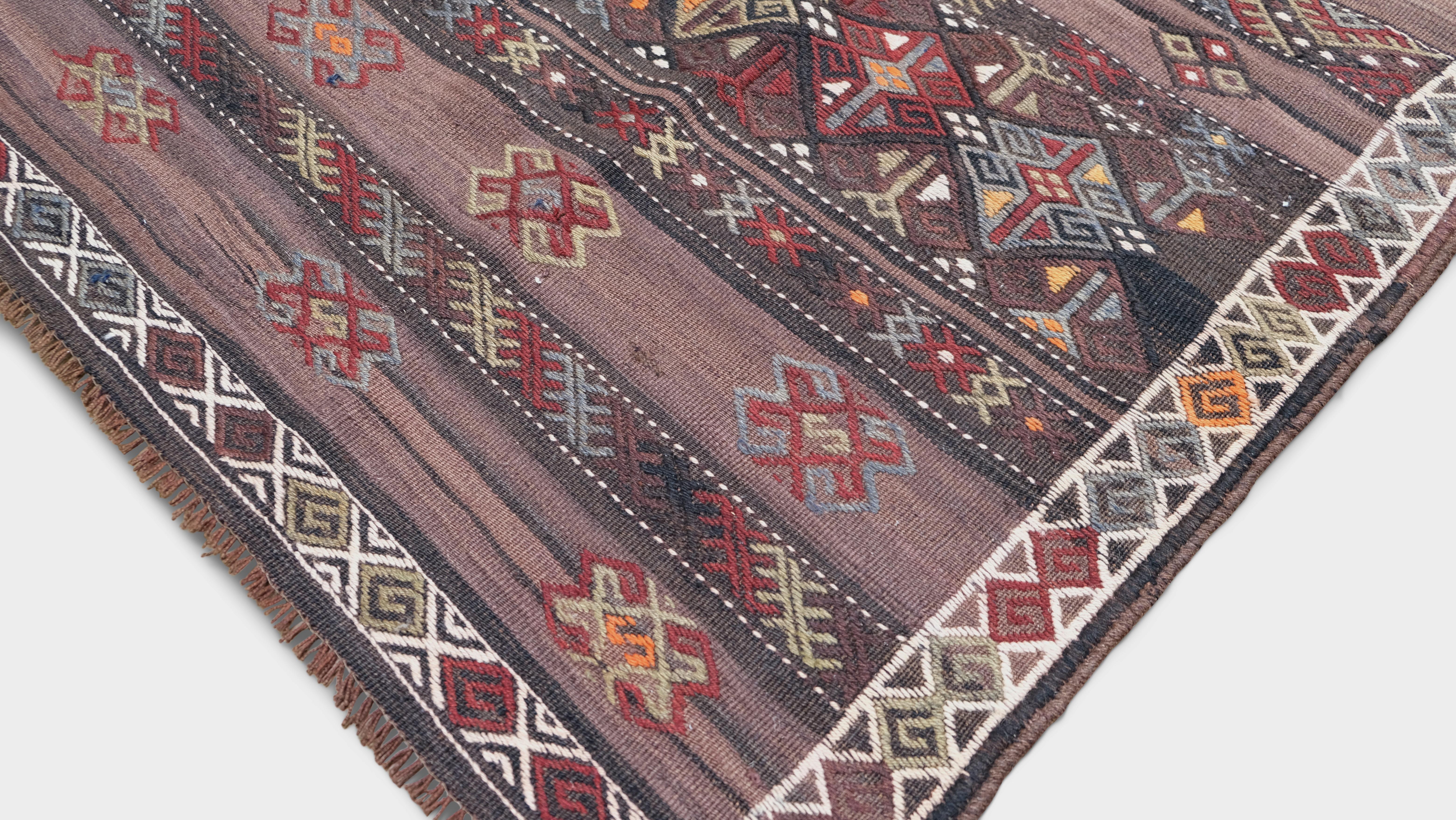 Elevate your space with this stunning vintage hand-woven wool rug. Featuring a bold geometric tribal motif, this piece boasts intricate patterns in a rich palette of earthy red, plum and blue tones, accented by subtle hints of orange. The rhythmic