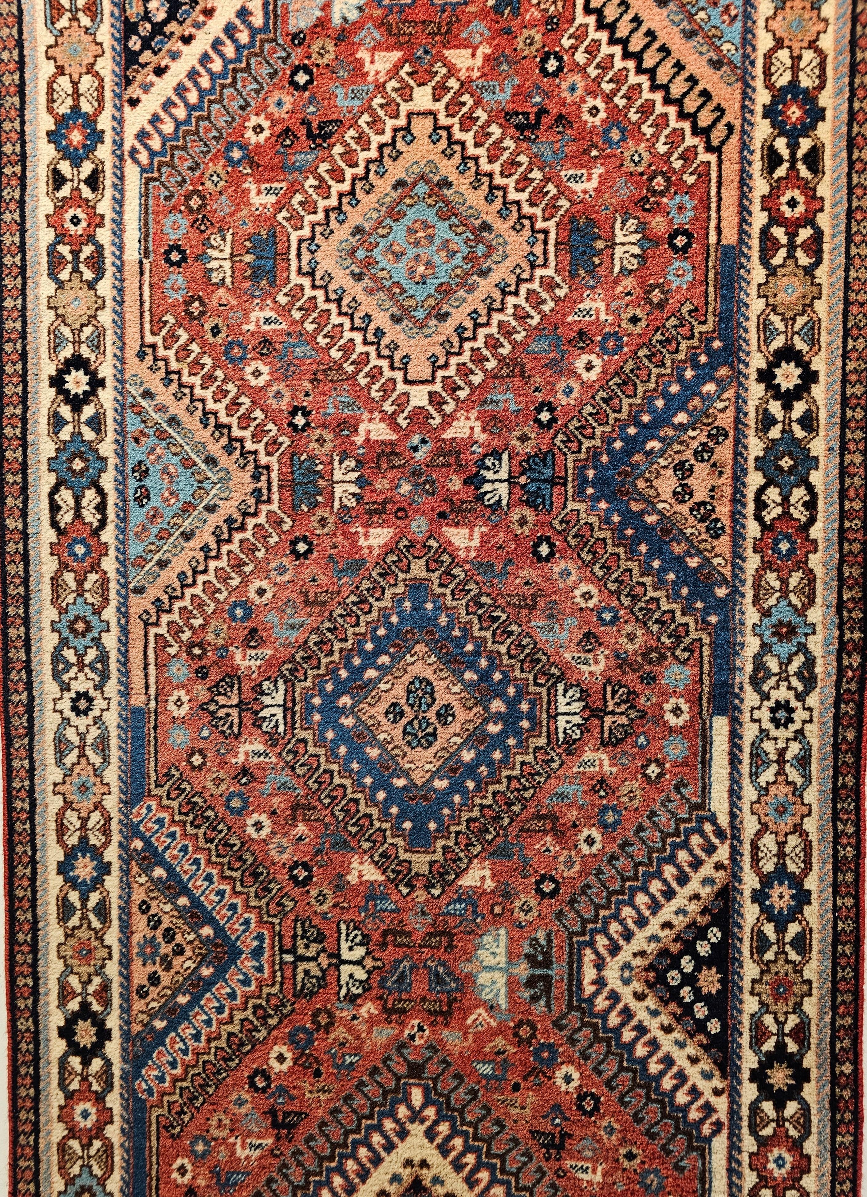 A beautiful vintage Persian Shiraz Yalameh tribal runner in a geometric allover pattern in red, ivory, and blue colors.  The design consists of a single column of connected latch hook medallions in bright colors of yellow, and red set on a French