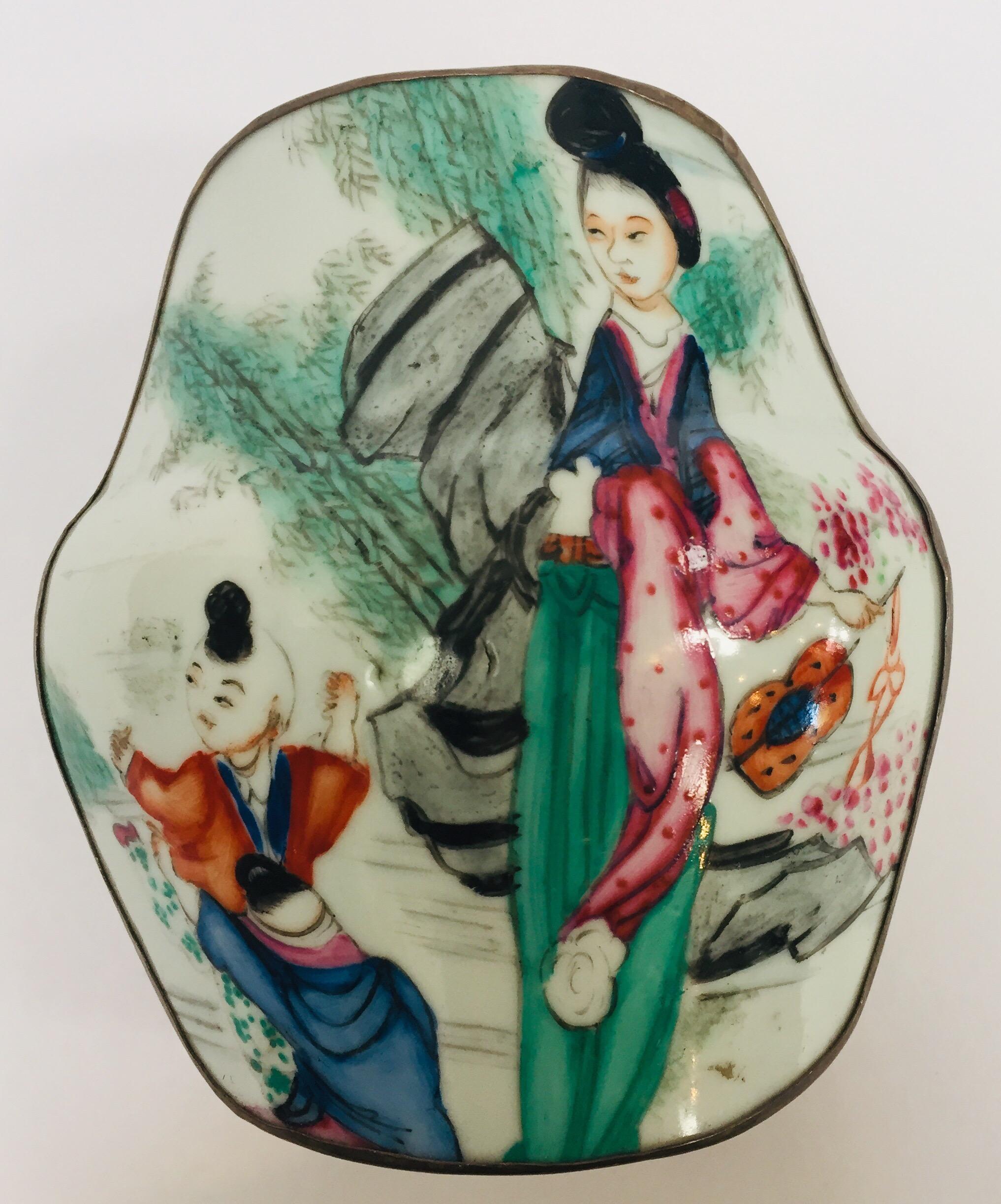 Vintage metal and porcelain trinket box with hand painted Asian Japanese scene.
Metal silvered with porcelain top hand painted with an outdoor scene with a mother and child wearing traditional kimonos in pink, green and blue colors.
Dimensions: