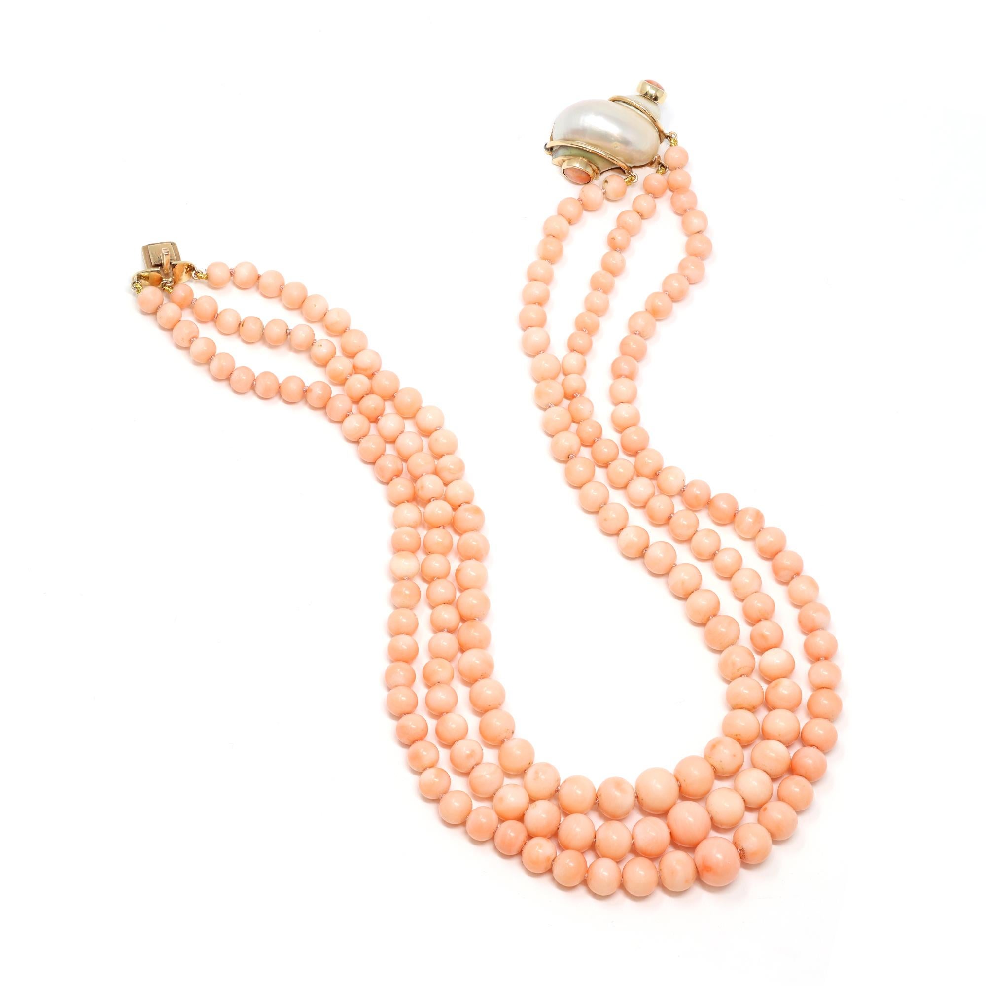 An original vintage and rare coral necklace featuring angel skin coral beads, set as triple strands, with a unique shell clasp displaying matching coral cabochon on both ends. The coral beads are natural with no indication of dye. The necklace has a