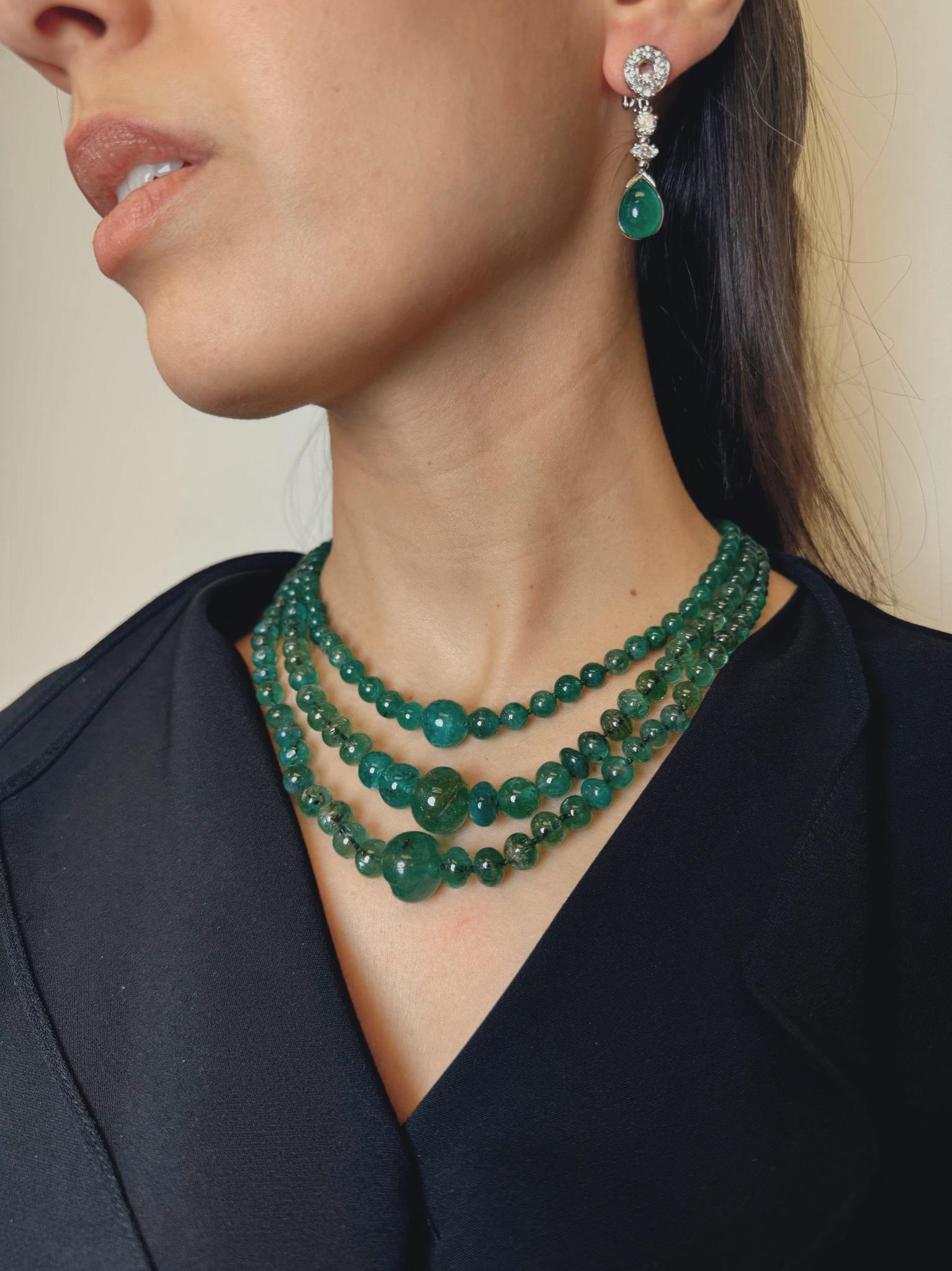 A breathtaking vintage triple-strand necklace composed of richly hued natural emerald beads, elegantly graduated in size for a flowing, layered silhouette. The necklace is strung on silk cord and culminates in an exquisite platinum diamond clasp