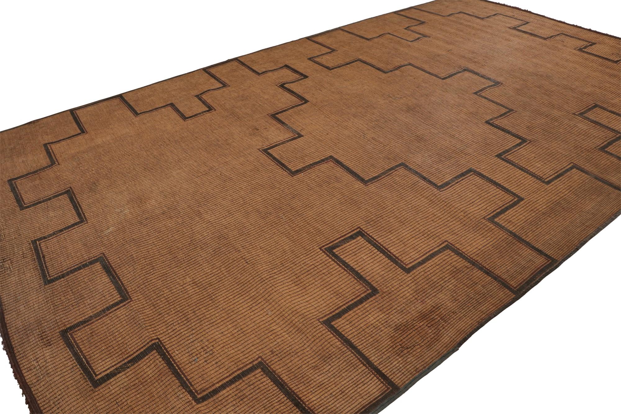 Hand-woven in reed and leather circa 1940-1950, this 10x16 vintage Tuareg Moroccan area rug is from the nomadic tribe of the same name. A rare large-size selection, its design enjoys warm beige undertones and rich brown geometric patterns in