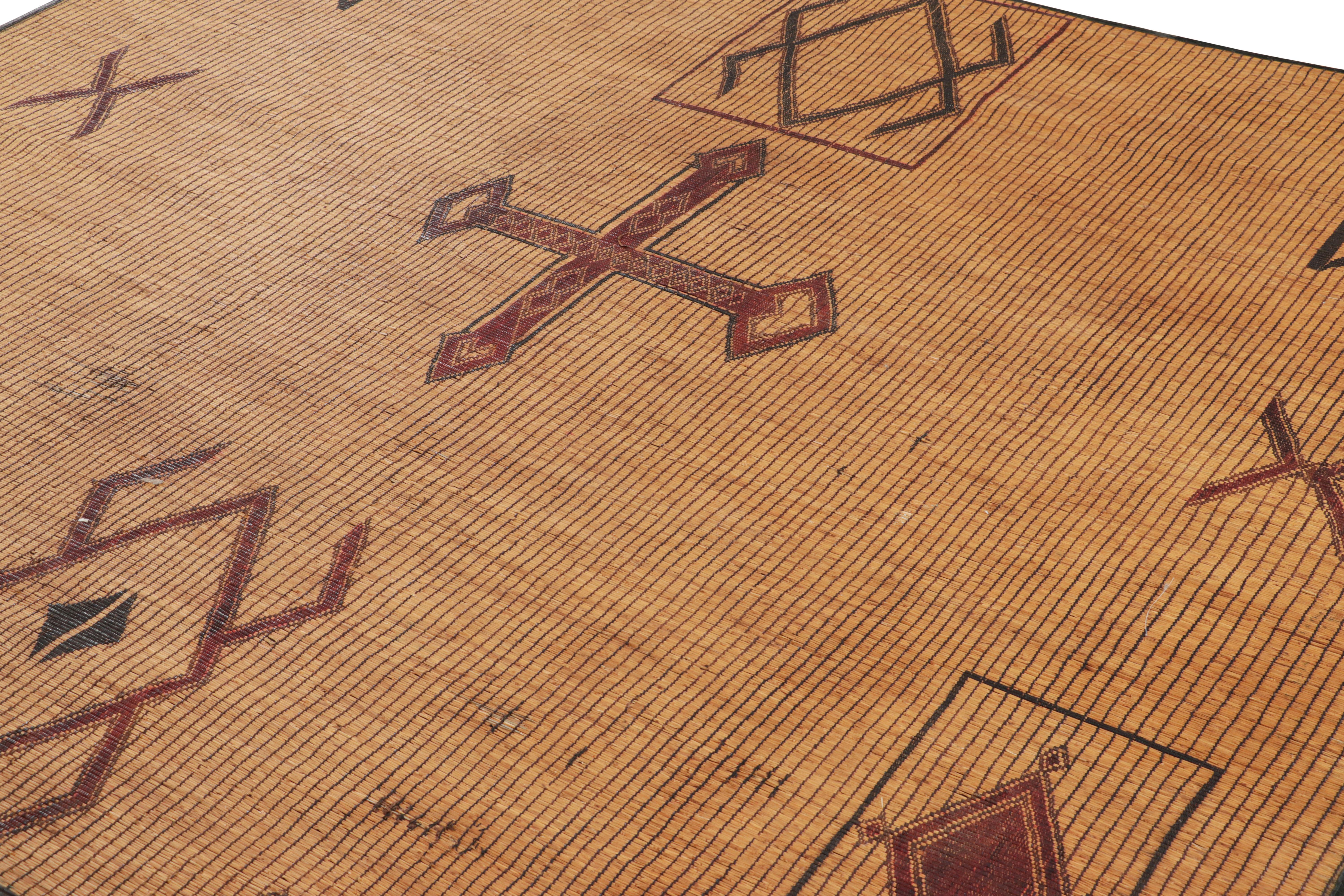 This vintage rug and floor covering is a 7x8 Tuareg mat from the nomadic tribe of the same name. Handwoven with reeds and camel leather in Mauritania circa 1950-1960, its natural materials enjoy beige-brown, red, black and cream tones in its