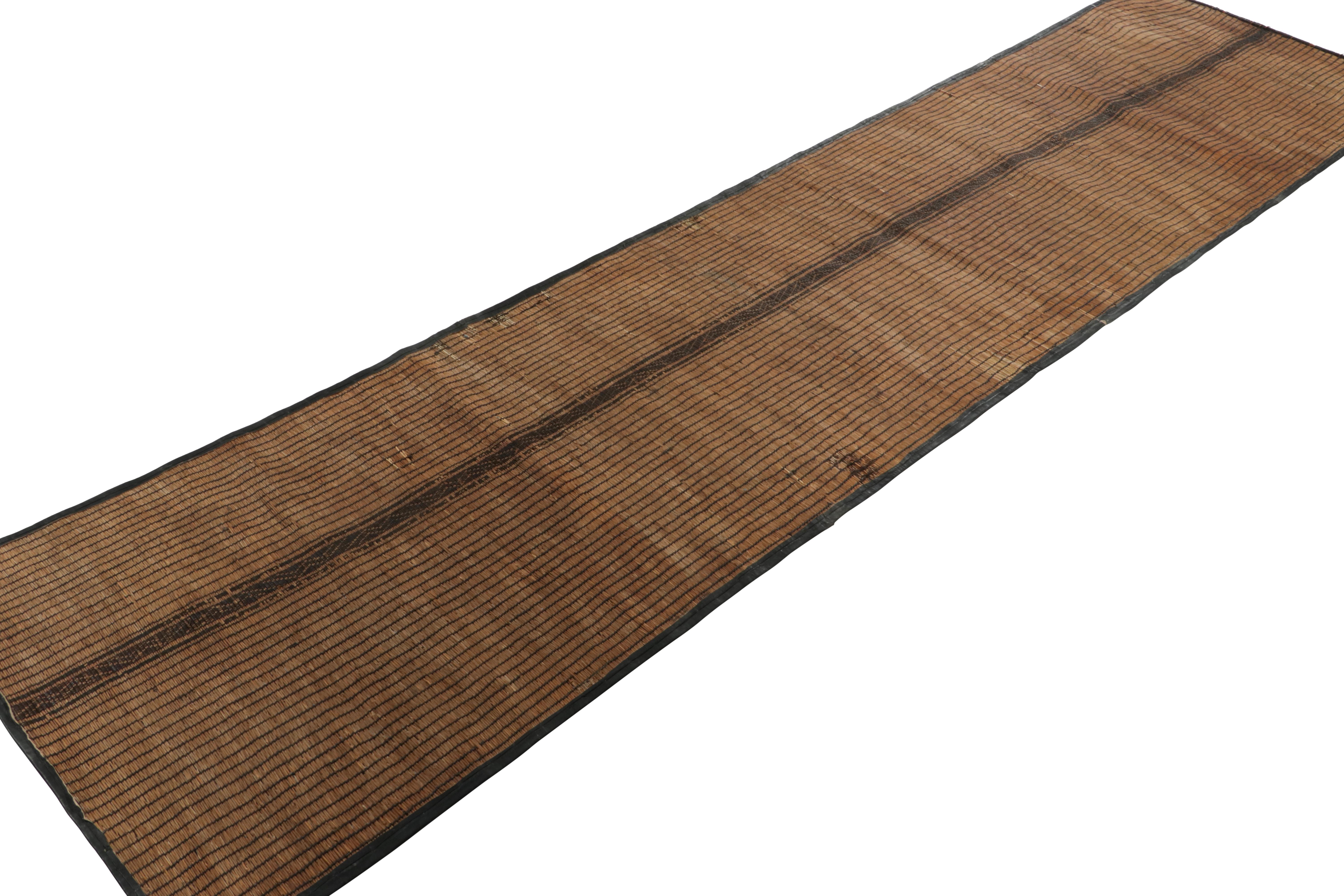 This vintage runner rug and floor covering is a 3x12 Tuareg mat from the nomadic tribe of the same name. Handwoven with reeds and camel leather in Mauritania circa 1950-1960, its natural materials enjoy beige-brown, black and cream tones in its