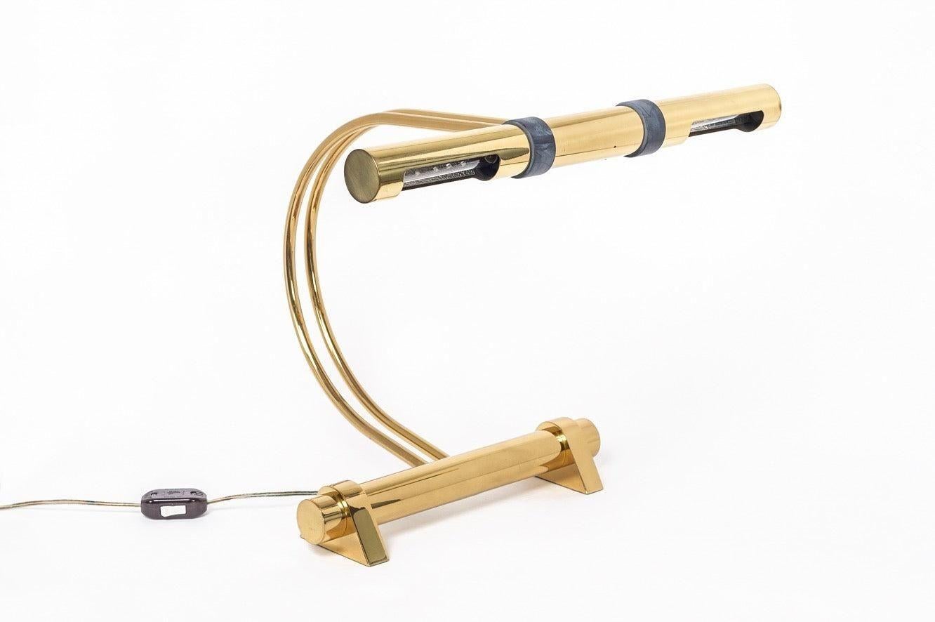 Esta excepcional lámpara de sobremesa modernista de latón pulido de Casella Lighting, de hacia 1970, tiene dos casquillos con pantallas tubulares sostenidas por un vástago de doble arco sobre una base cilíndrica. Las pantallas tubulares son