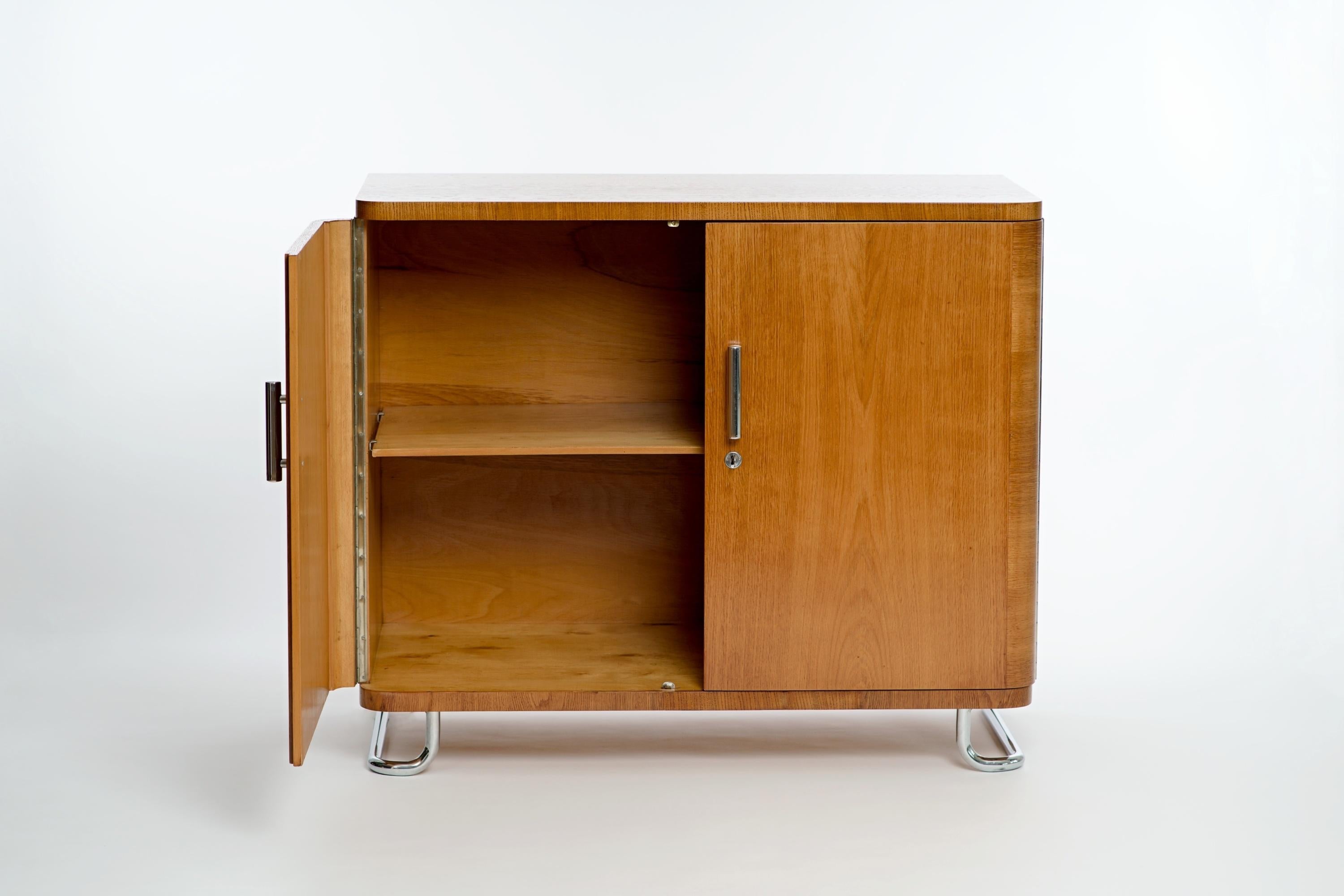 This 2-door sideboard made of oak veneer was made in the former Czechoslovakia in the 1950s. Chromed tubular steel feet and handles. Designed in 1935, executed in the early 1950s. Beautiful restored vintage condition.