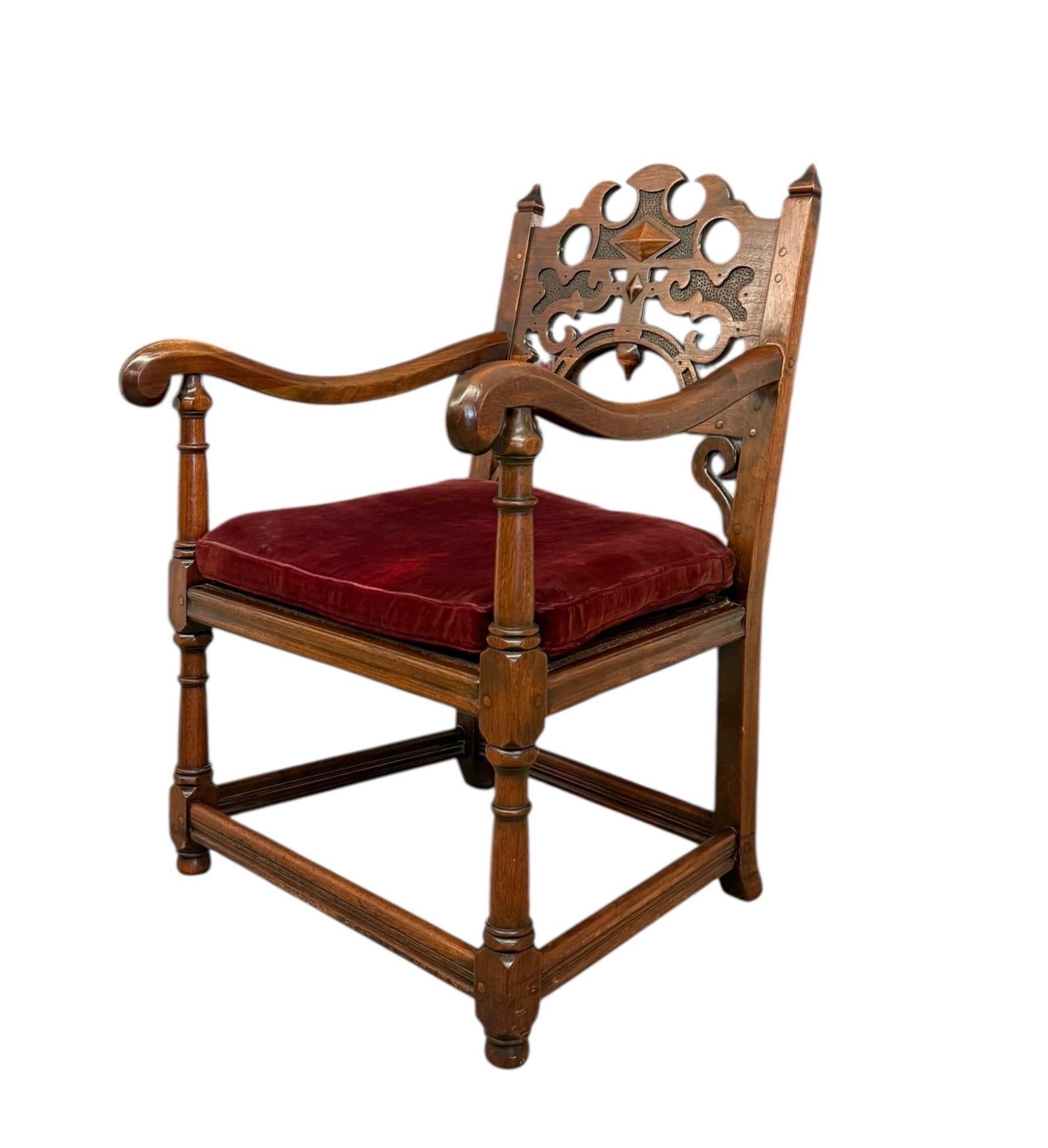 La sedia vintage è realizzata in legno scuro con uno stile Gothic Revival, evidente nei suoi intricati intagli, tra cui ritagli circolari, motivi a vortice e un intarsio a forma di diamante sullo schienale. Lo schienale alto e arcuato, con la parte