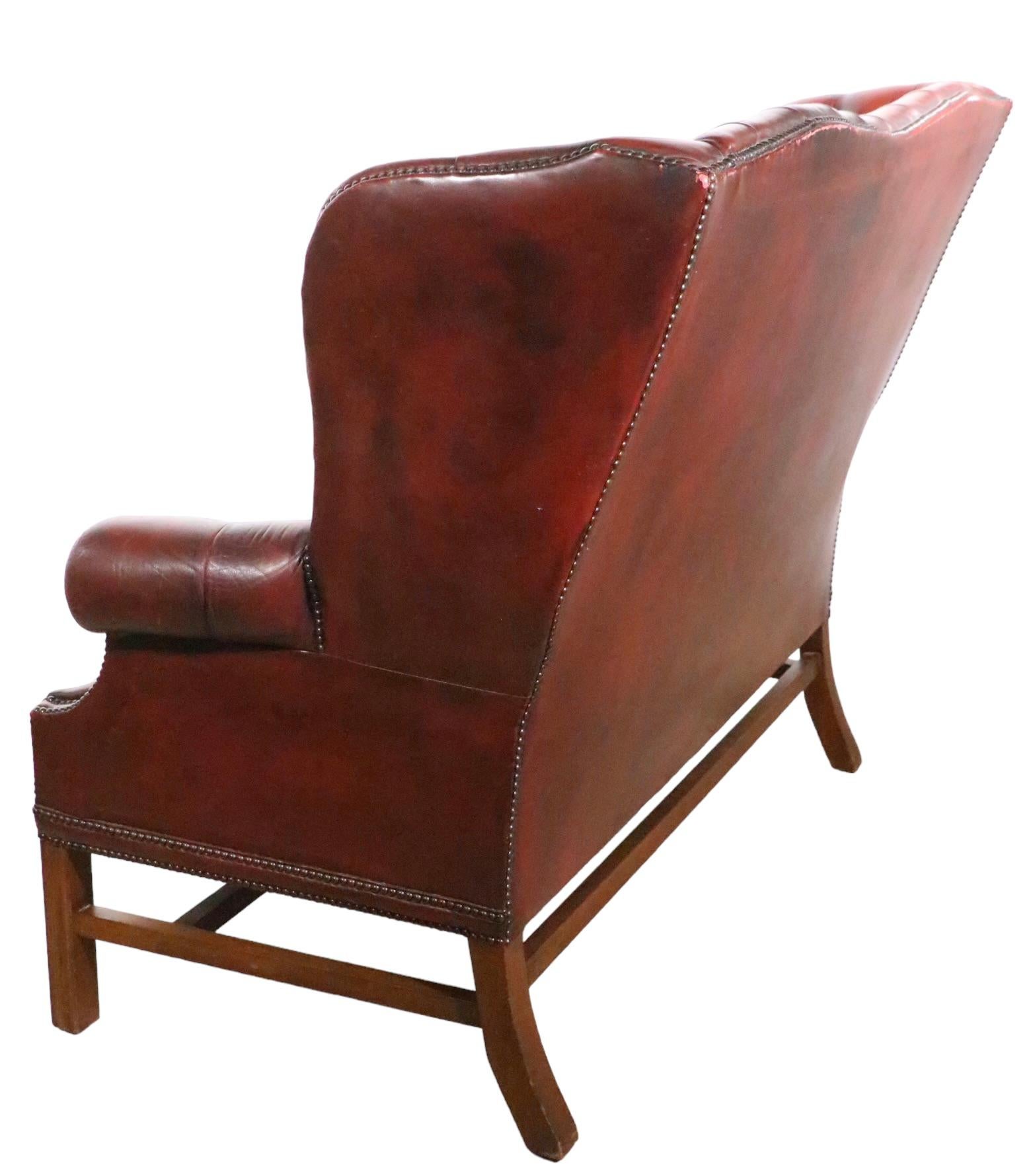 Voguish tufted leather wingback style loveseat, on solid wood legs. Classic English Chippendale style, circa Mid 20th C, well crafted, iconic and timeless design, still relevant to today’s interior spaces. This exceptional sofa is in very fine