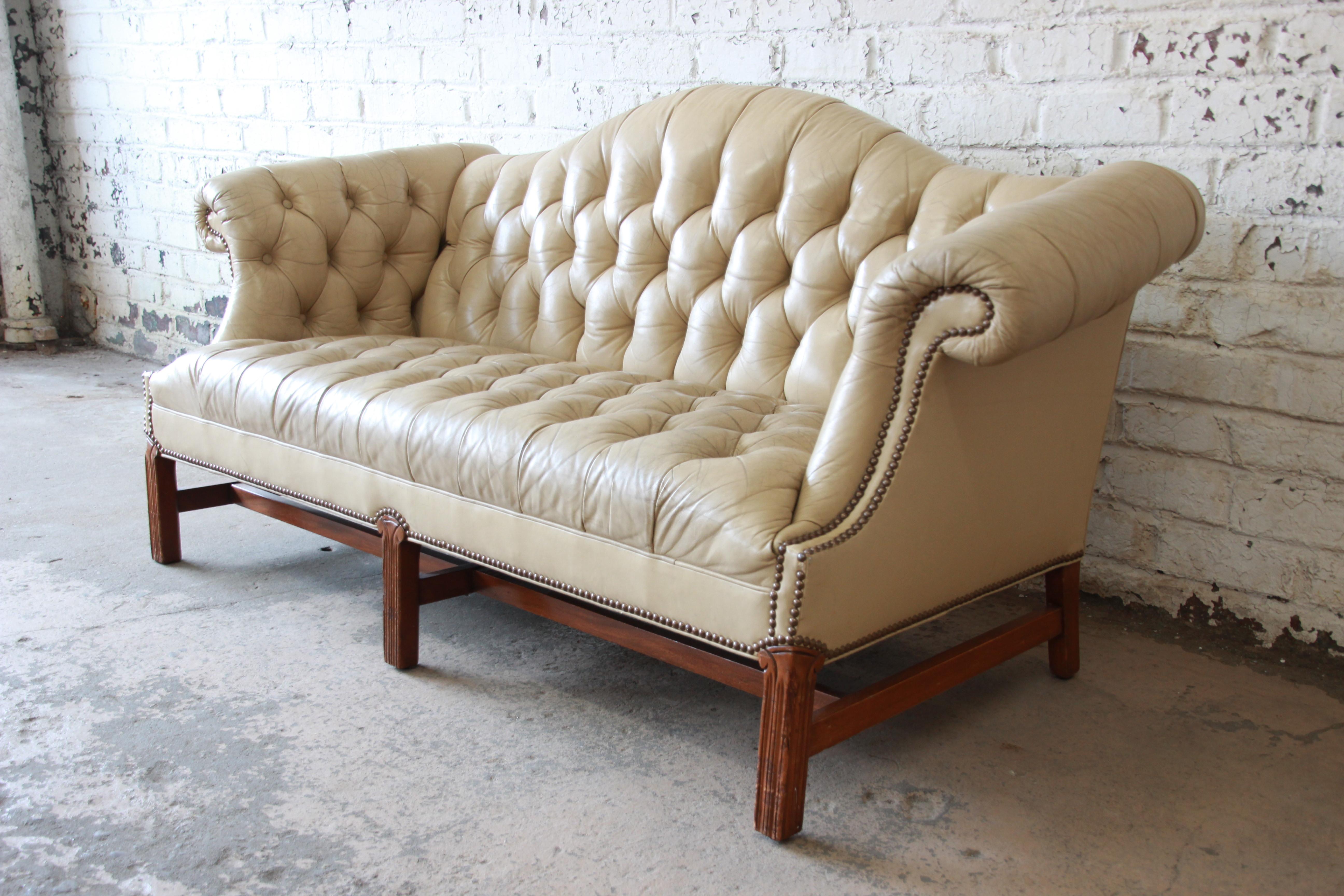 An exceptional vintage tufted tan leather Chesterfield style sofa. The sofa features beautifully aged and distressed tan leather, brass nailhead trim, and scrolled arms. It sits on solid carved walnut legs, with walnut stretchers. Seat height is