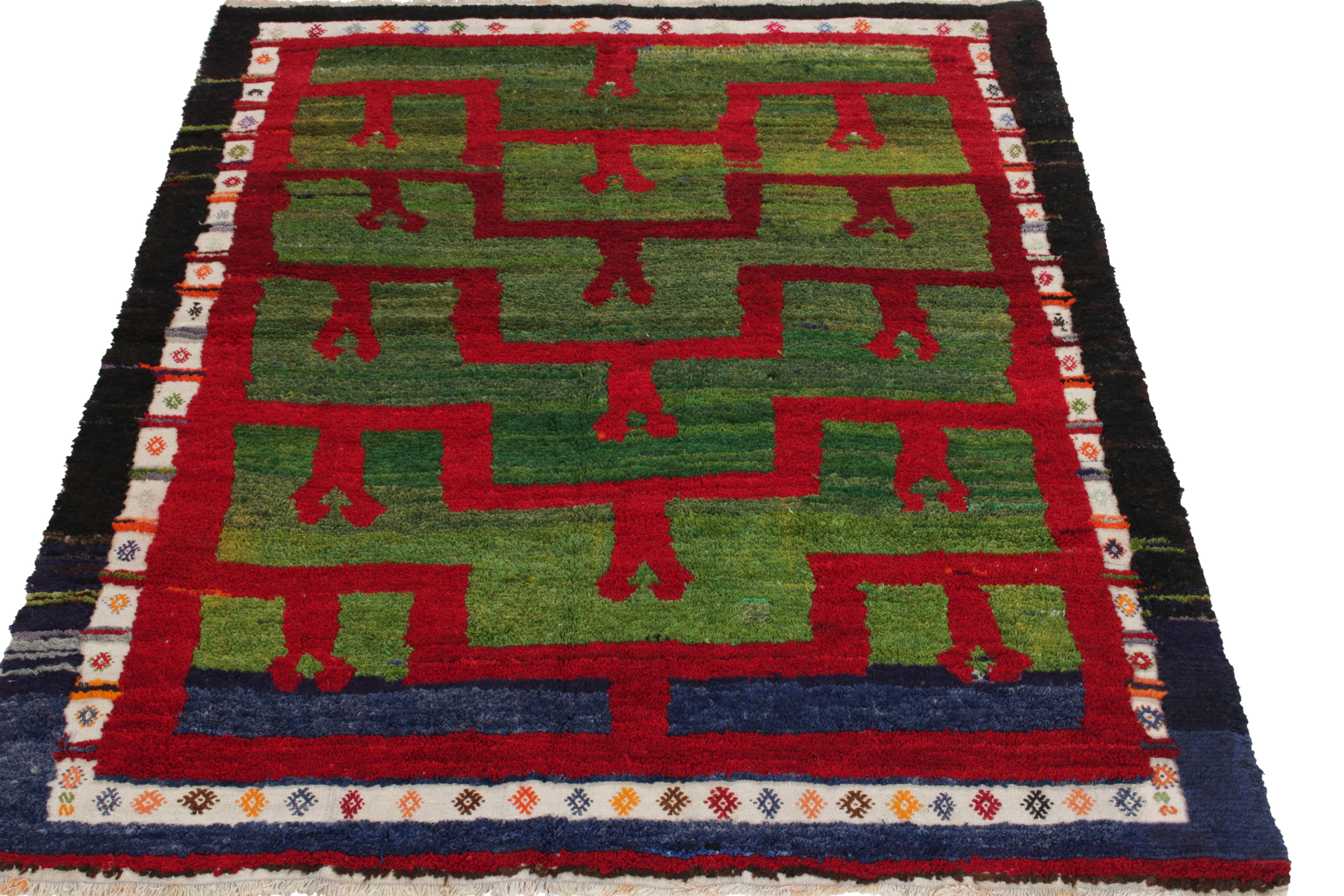 Hand-knotted in wool from Turkey circa 1950-1960, a vintage 5x6 Tulu rug from our Antique & Vintage collection celebrating the period style through a symmetric geometric pattern—bold red tones in play with striated green hues, enfolded in a white
