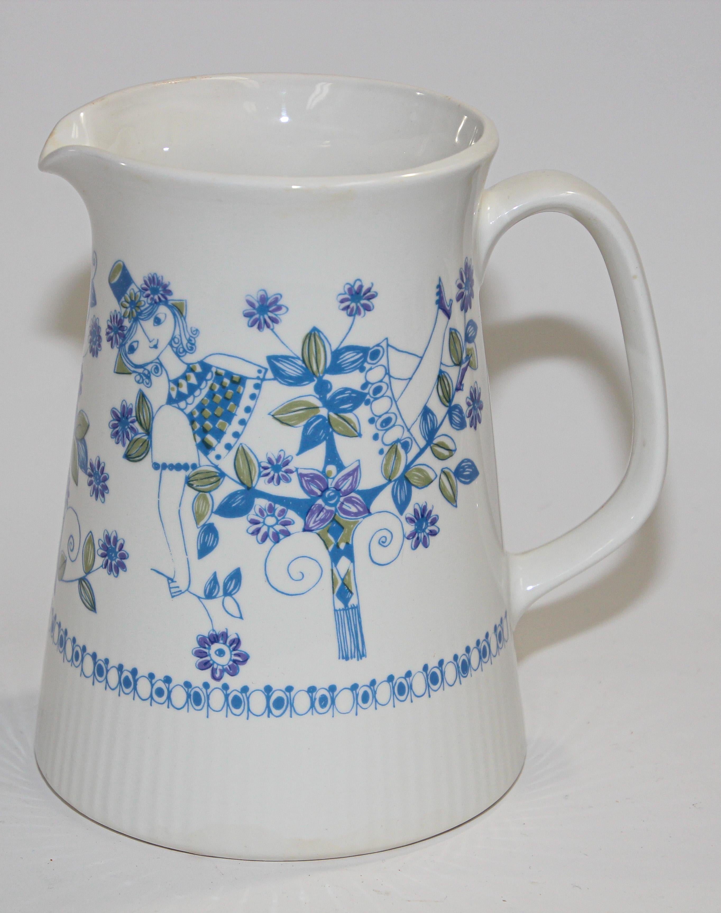 Vintage Turi-Design Lotte hand painted pitcher, Made in Norway, stamped 1075 on Bottom, F/F Figgjo Flint Flameware, # 1075.
The pitcher is high gloss white ceramic with a girl wearing a flower hat relaxing in a floral garden. The blue and olive