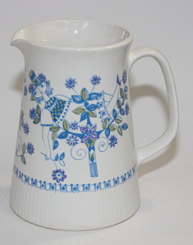 Vintage Turi-Design Lotte hand painted pitcher, Made in Norway, stamped 1075 on Bottom, F/F Figgjo Flint Flameware, # 1075.
The pitcher is high gloss white ceramic with a girl wearing a flower hat relaxing in a floral garden. The blue and olive