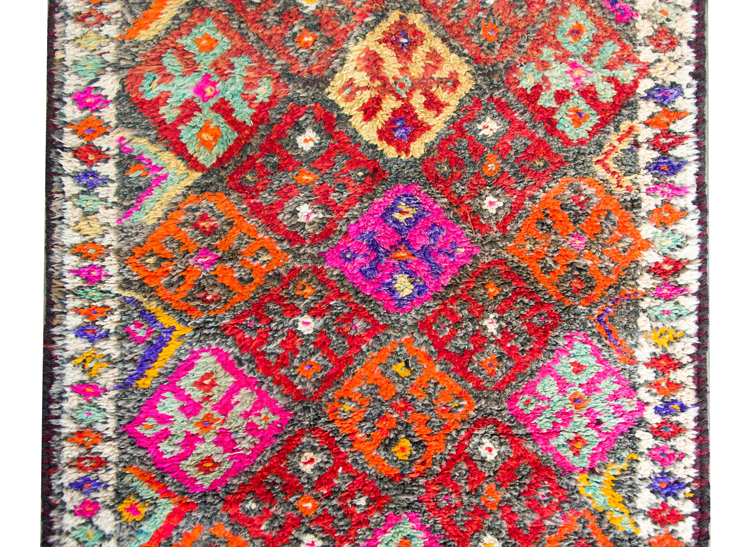 A striking late 20th century Turkish Anatolian kilim runner with an all-over repeated diamond pattern woven in brilliant oranges, pinks, violets, crimsons, and greens.