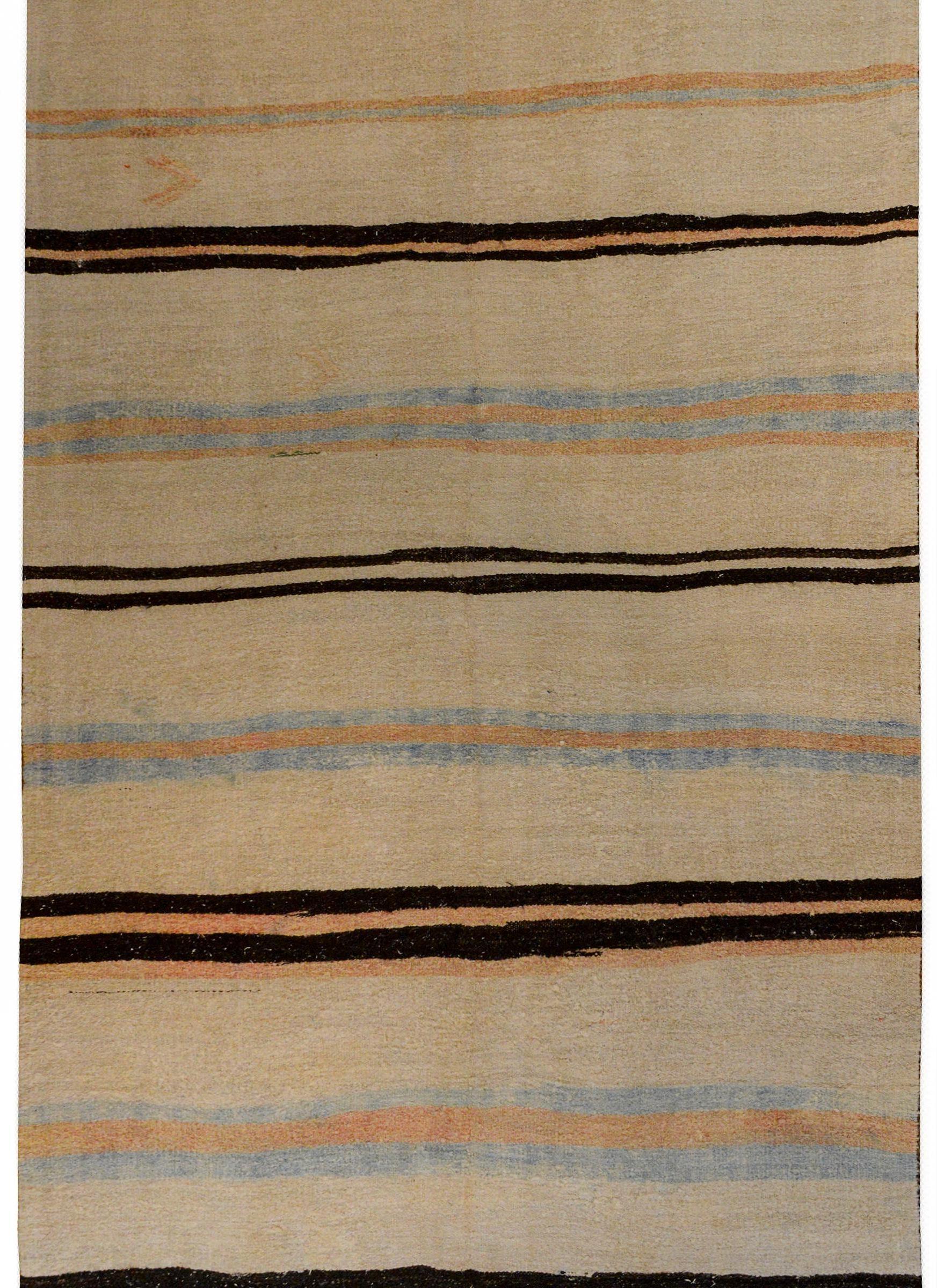 A beautiful vintage Turkish cotton kilim rug with a striped pattern containing black, pale indigo, and camel colored stripes on a cream background.