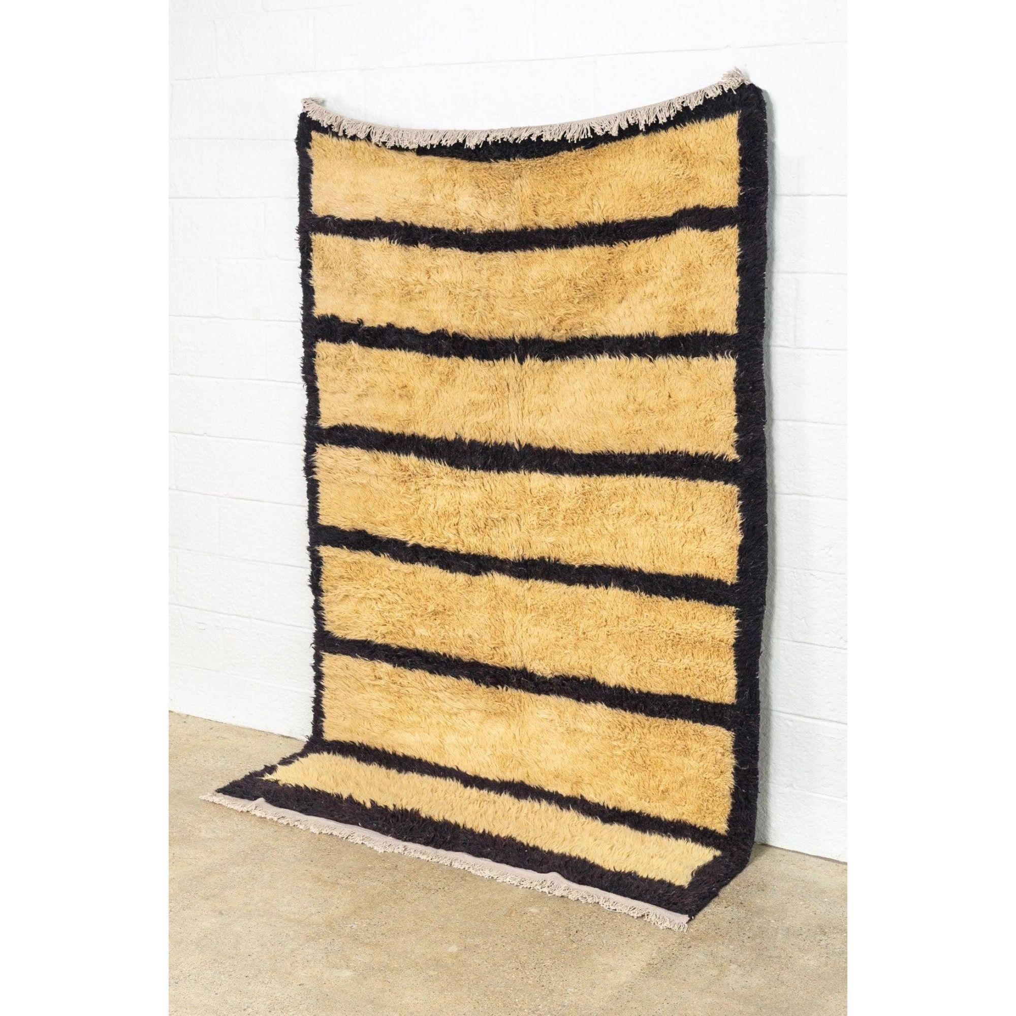 This vintage handwoven Anatolian wool floor rug features an abstract, Minimalist design with an open beige field and brown-black stripes and border edge. The shaggy wool pile is soft and luxurious and finished with a natural cotton warp fringe to