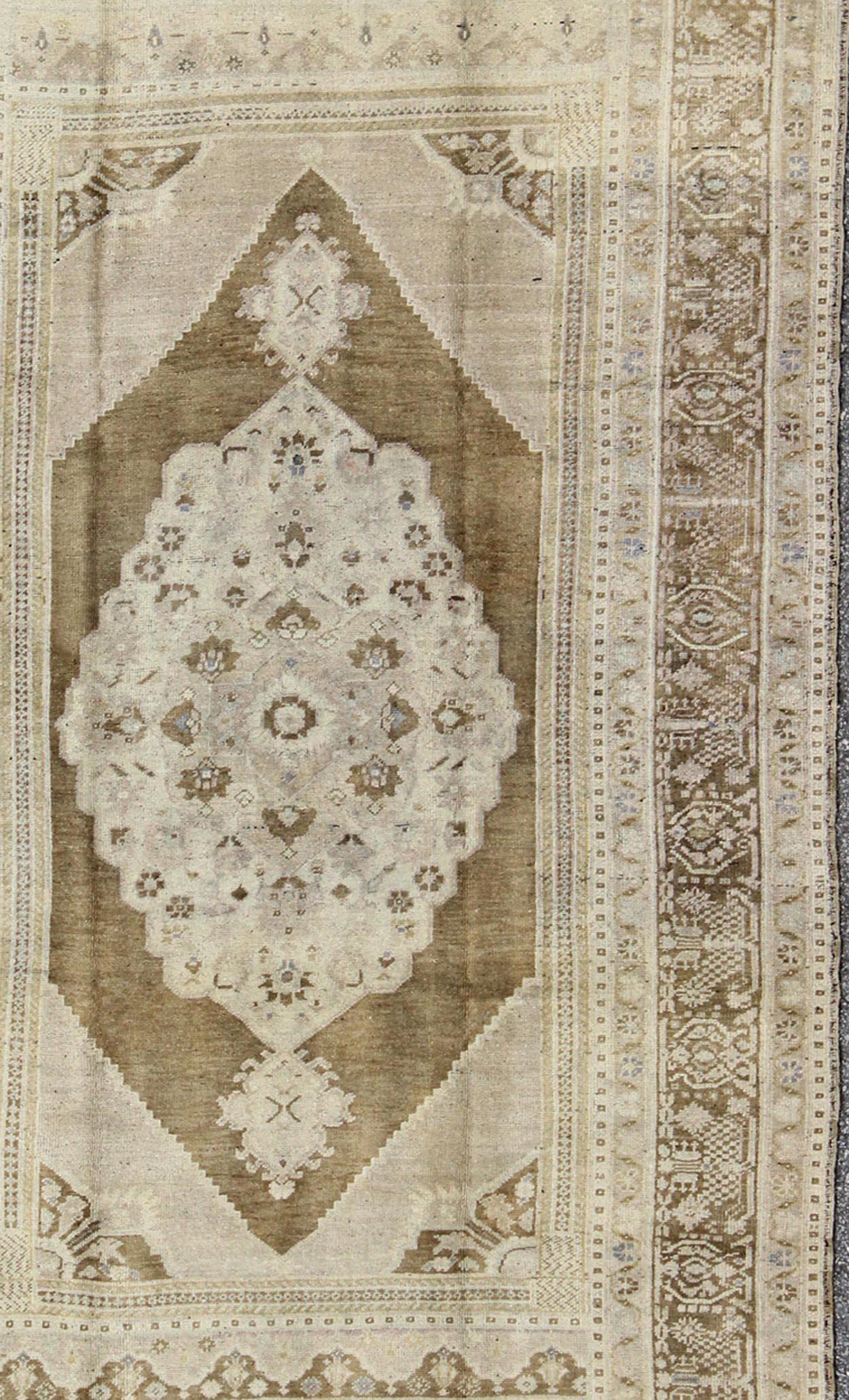 Measures: 5'11 x 9'6

Set on a khaki background and brown border, this vintage Turkish Oushak displays an unique earth tone color combination with various shades of taupe and army green along with hints of light blue and neutral colors. The border