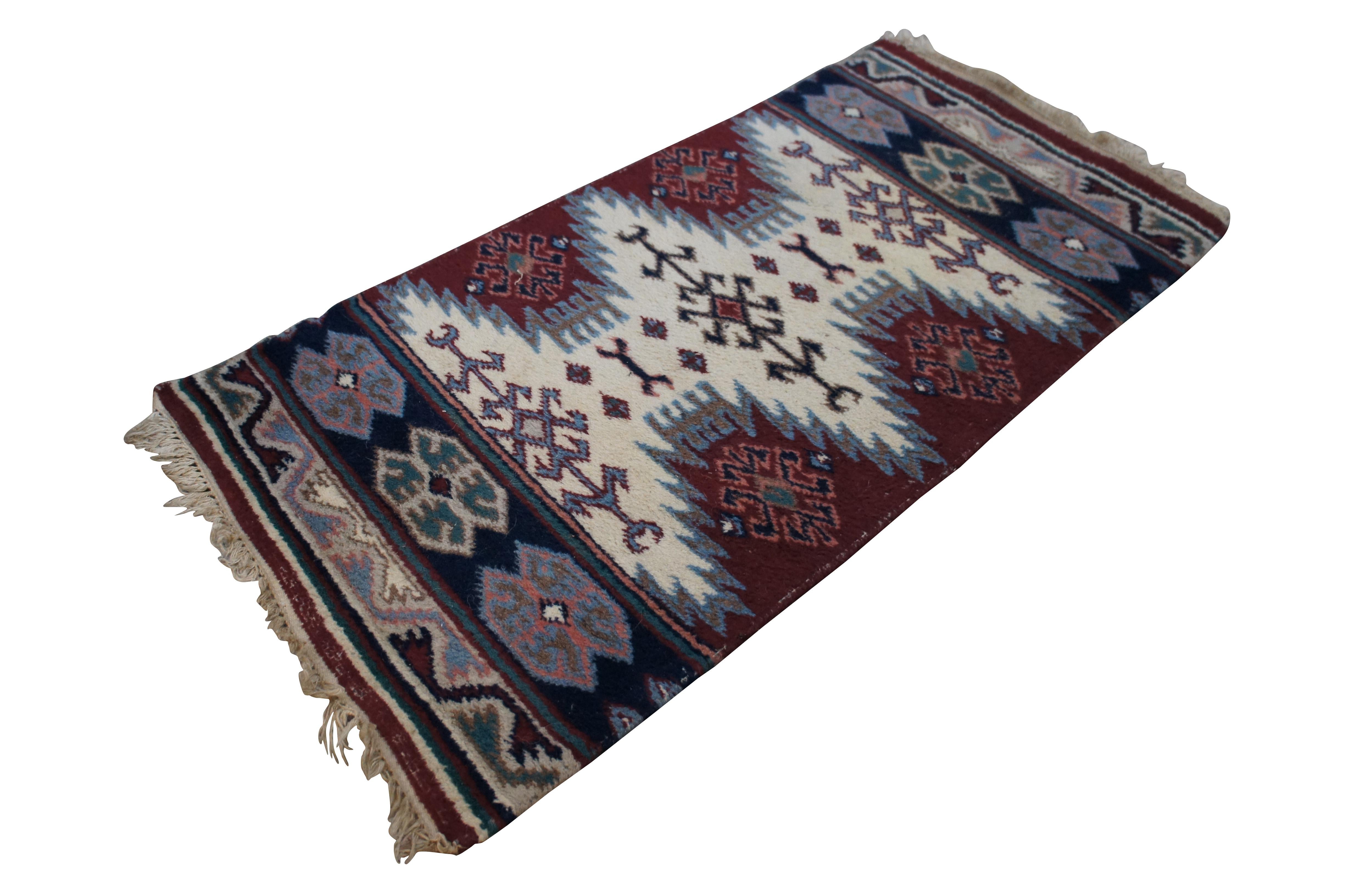 20th century small hand knotted Turkish wool rug / mat featuring a geometric pattern in red, cream, navy, blue, and pink. Rug sports a low pile, hand bound side edges and knotted fringe at the ends.

DIMENSIONS
55” x 27.5” / 4.6’ x 2.3’ (Length x
