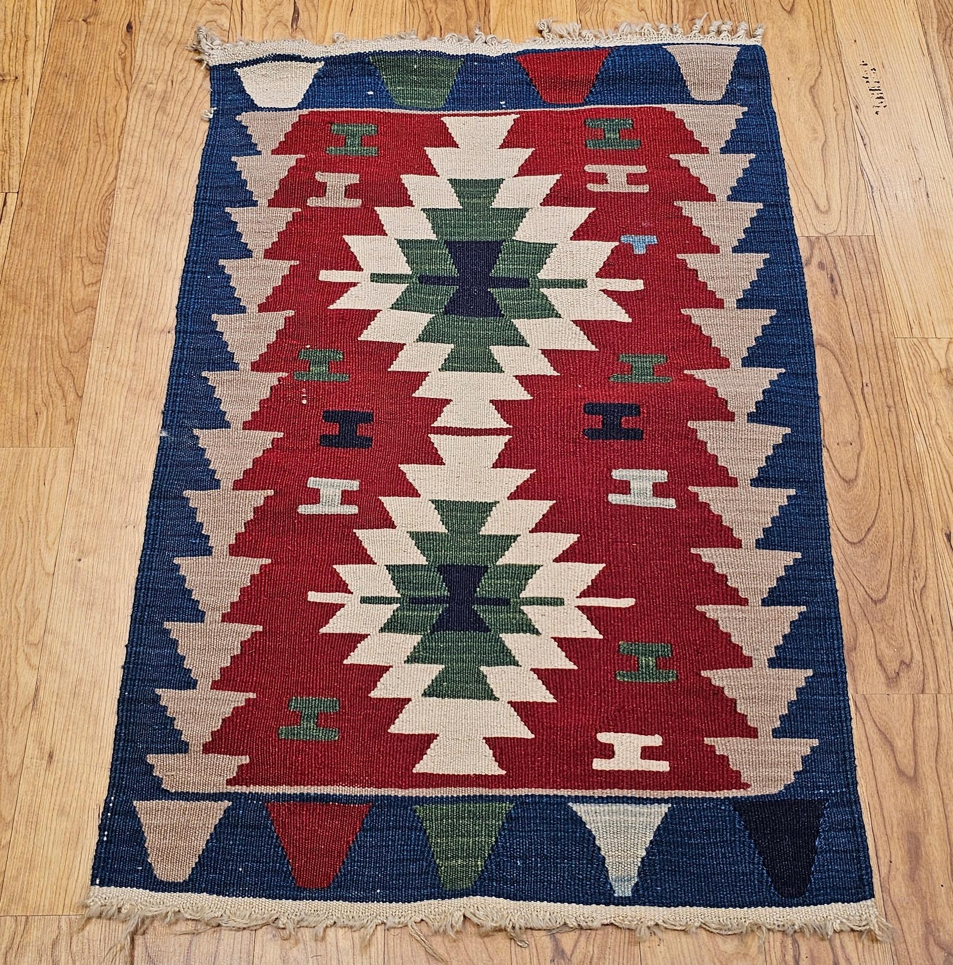 Magnifique et coloré tapis kilim turc tissé à la main datant du milieu des années 1900.  Le kilim présente un motif géométrique en médaillon avec un fond rouge et deux médaillons de couleur ivoire, verte et marine.  L'utilisation de teintures