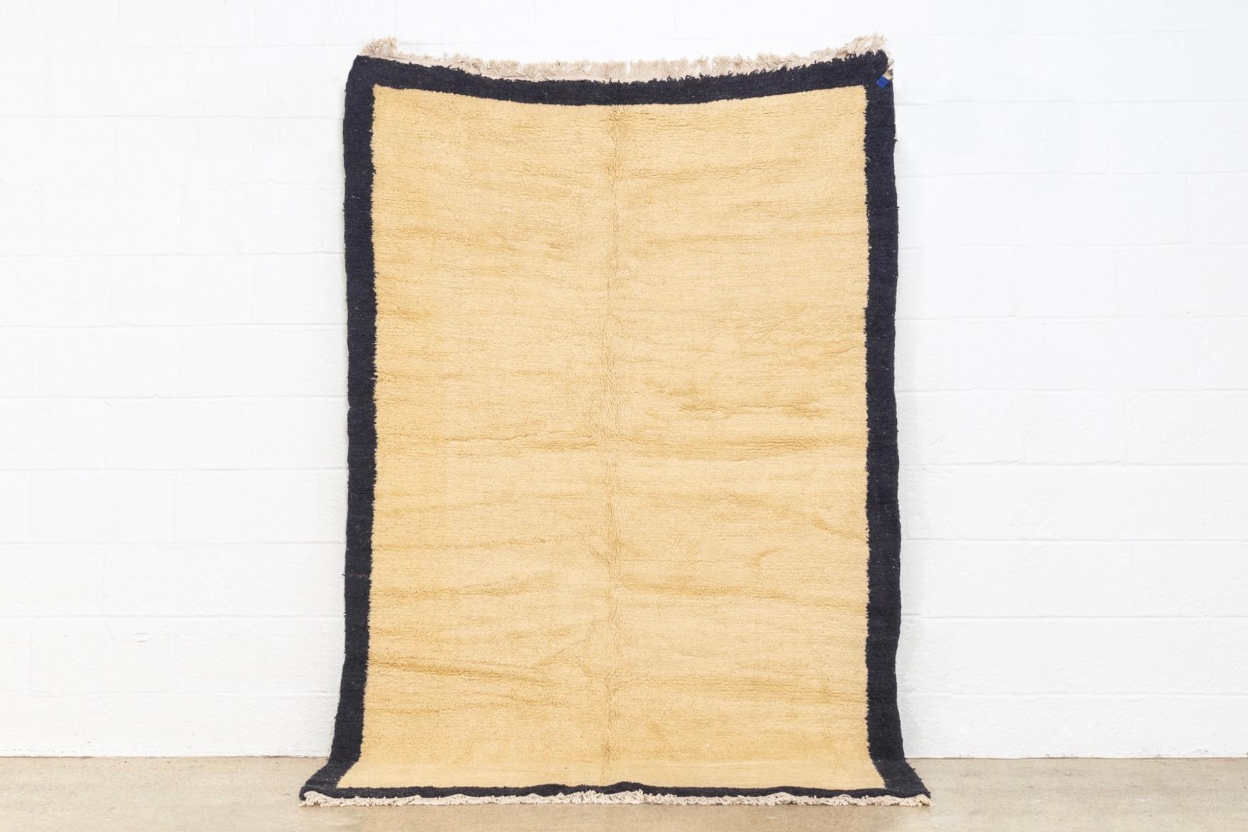 This vintage handwoven Anatolian wool floor rug features an abstract, minimalist design with an open oatmeal tan field within a solid black border. The medium wool pile is finished with a natural cotton warp fringe to both ends. This authentic