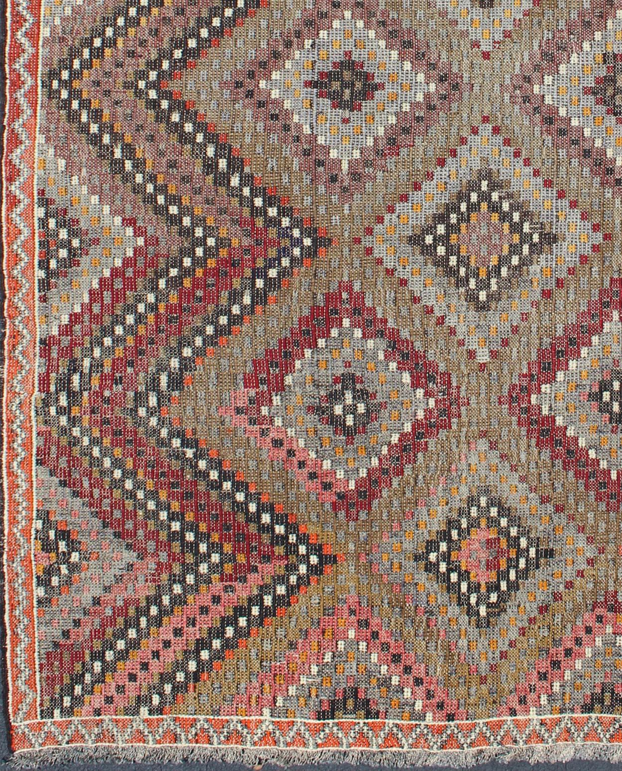 Measures: 6'5 x 10'2.
This Turkish embroidered Jajeem displays a repeating diamond pattern in the field and a simple zig-zag border. The taupe in the center gives this rug a neutral background. The other colors include shades of green, red, orange,