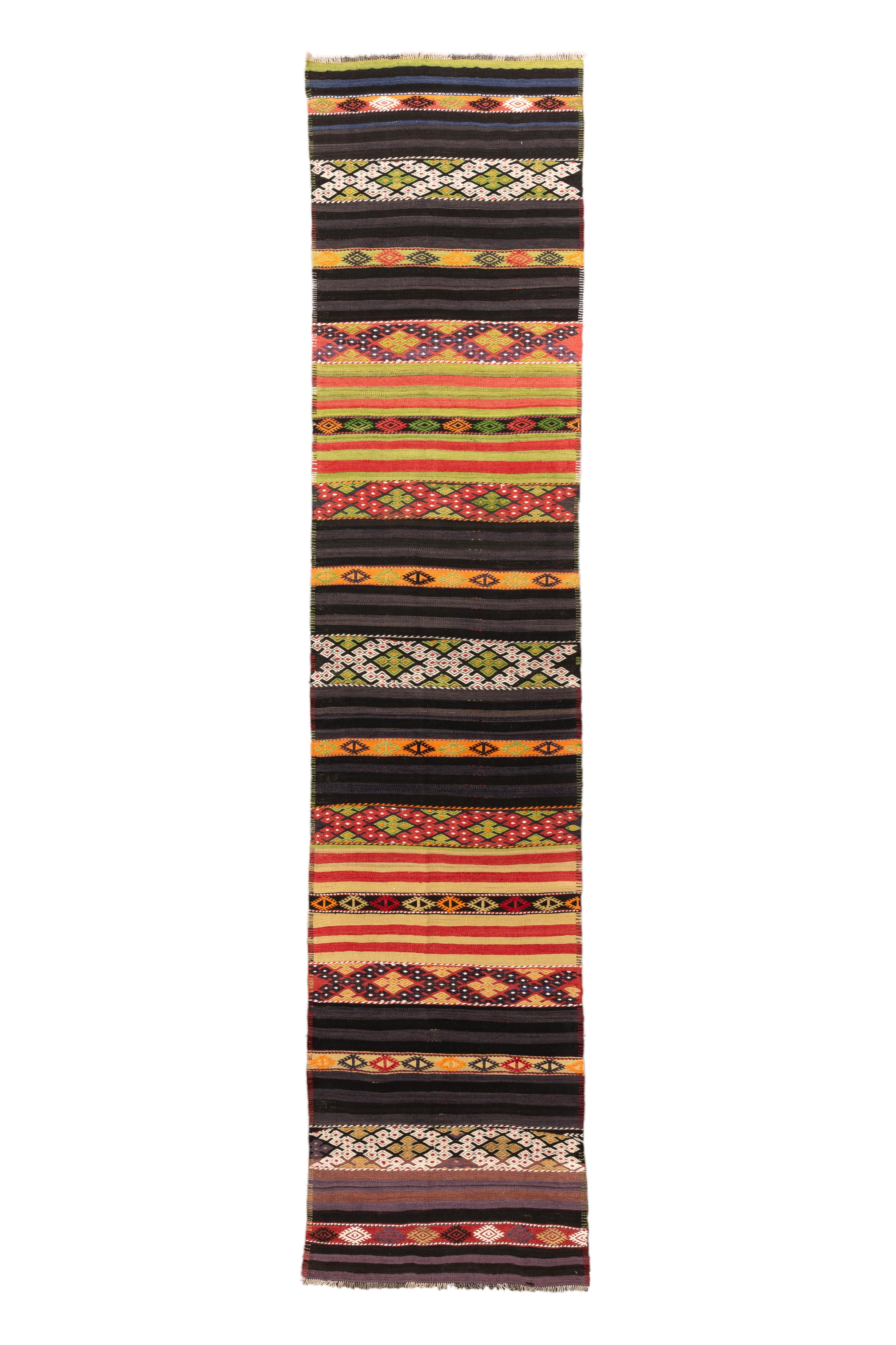  Un runner turco Jijim vintage, vibrante e ricco di texture, caratterizzato da un'esuberante combinazione di bande orizzontali in vivaci colori tribali. Tessuto a strisce alternate di nero, ocra, cremisi, avorio, oliva e mandarino, questo pezzo è