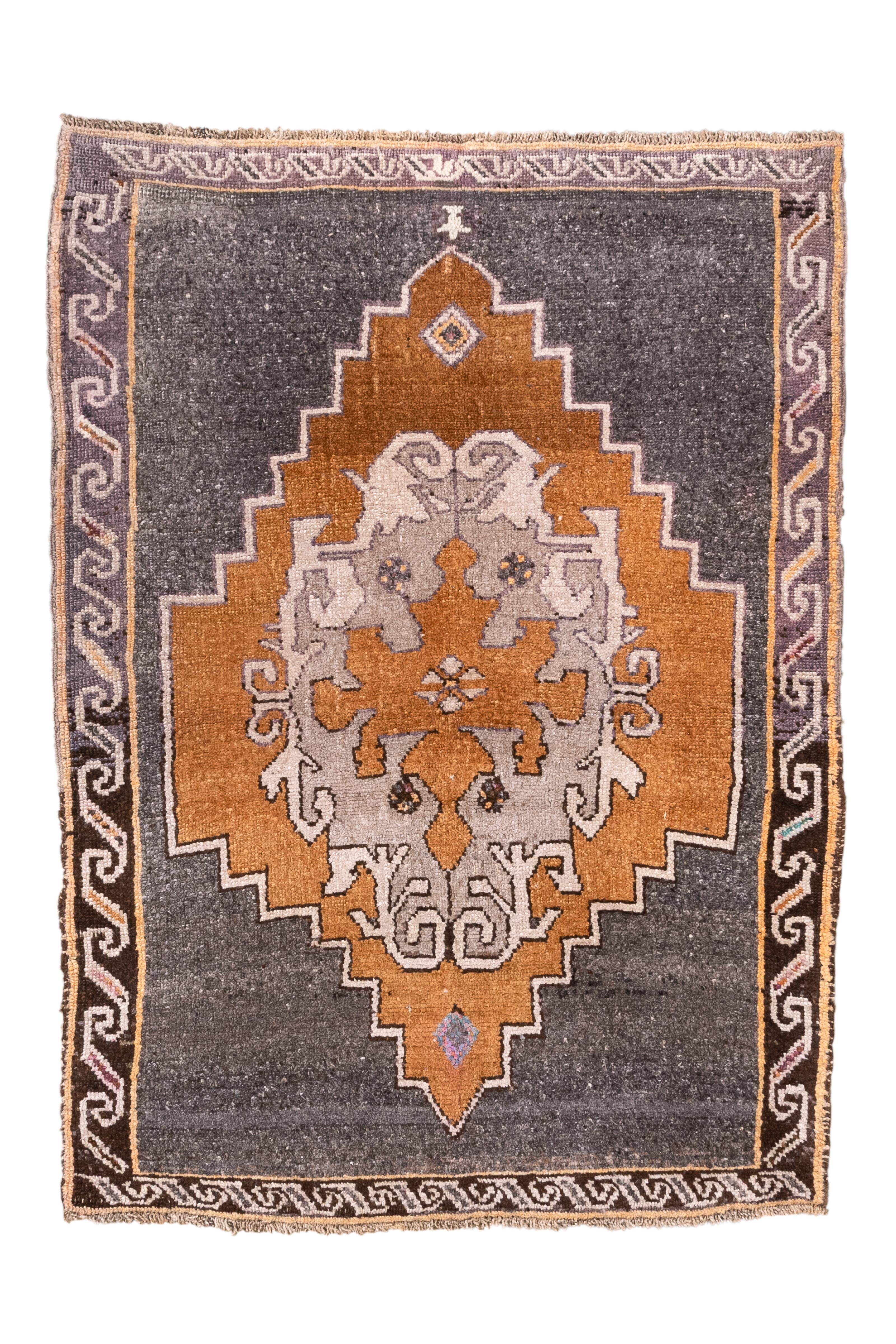A boldly graphic vintage Turkish Kars rug, handwoven in Eastern Anatolia in the mid-20th century. This rug features a striking large-scale medallion in warm amber-rust and soft gray against a charcoal black field, framed with geometric borders and