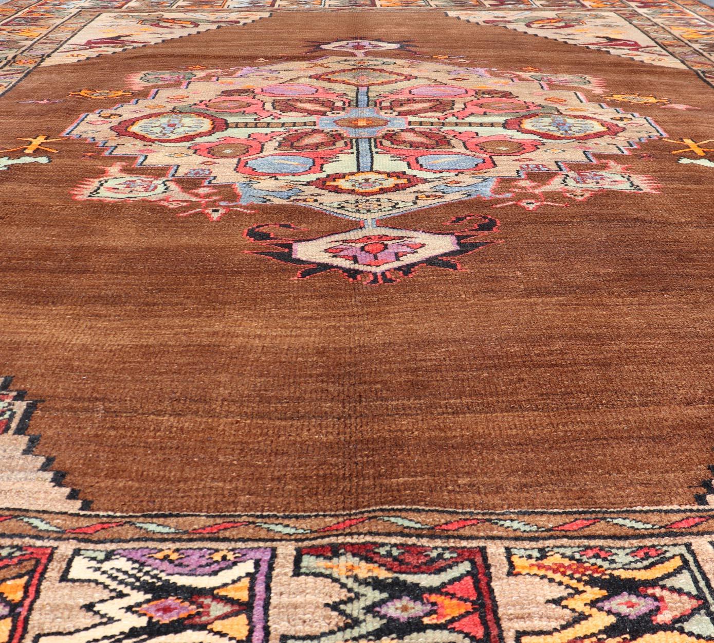 Vintage Turkish Kars Rug With Medallion On A Brown Field with Pops of Color. Keivan Woven Arts / rug / TU-MTU-3489, country of origin / type: Turkey / Oushak / Kars, circa 1940
Measures: 9'4 x 10'2.
This Turkish Kars rug has been handwoven in