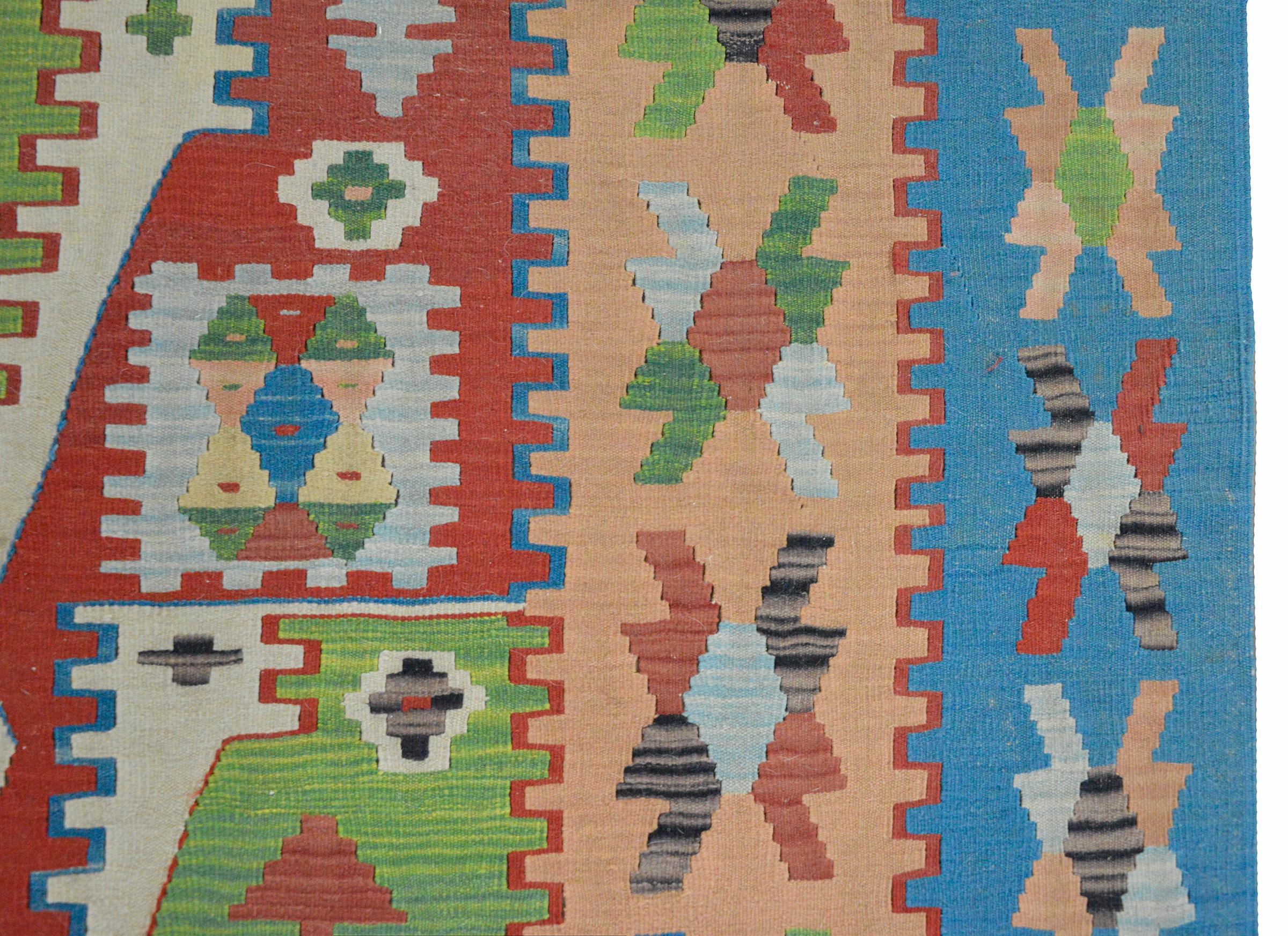A wonderful vintage Turkish kilim rug with a complex geometric pattern with myriad stylized flowers all woven in red, green, blue, and white, and surrounded by an exciting border with more stylized flowers.