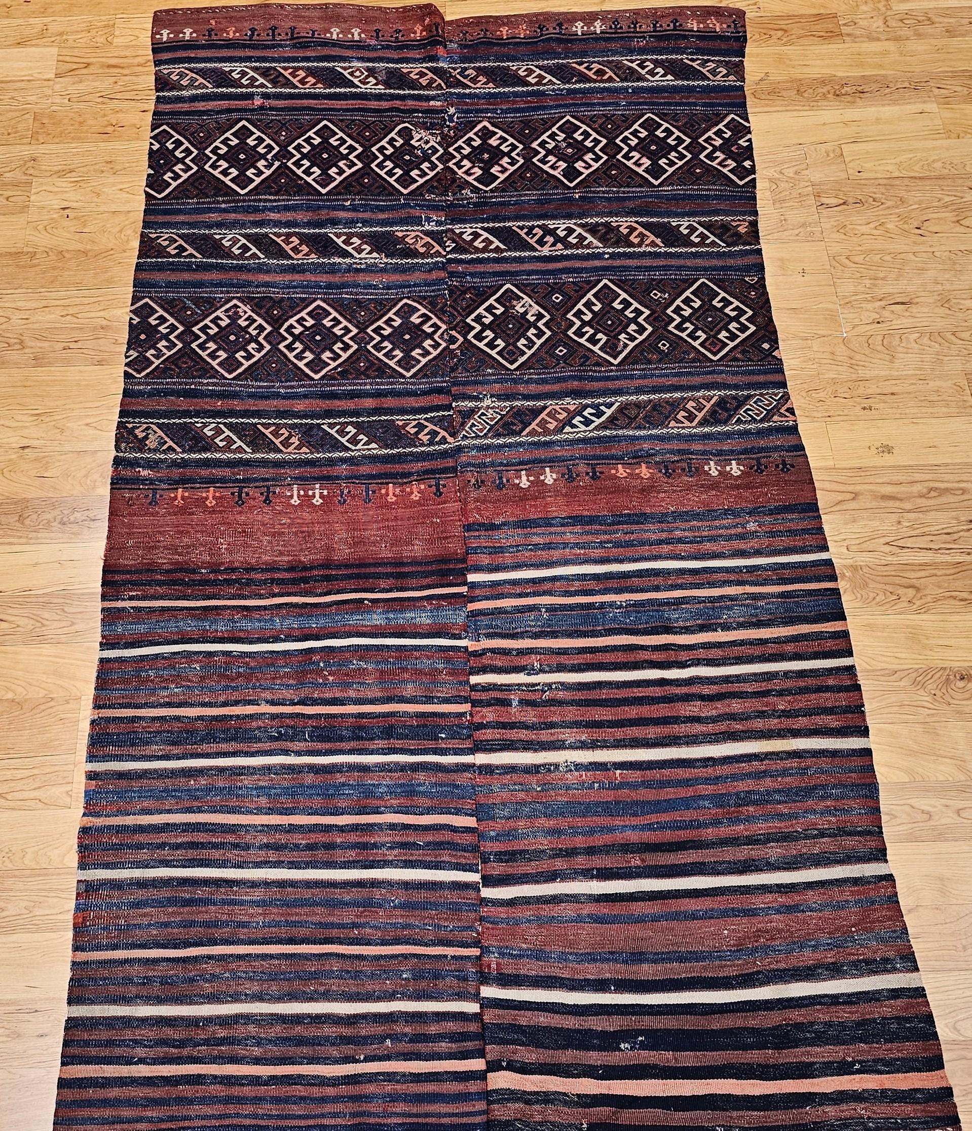 Vintage Turkish Kilim from the early 20th century in indigo blue, burgundy, ivory, and pink.  The kilim has traditional hooked star patterns in indigo blue set on a brick red or burgundy background color.  The designed stripes are  separated by