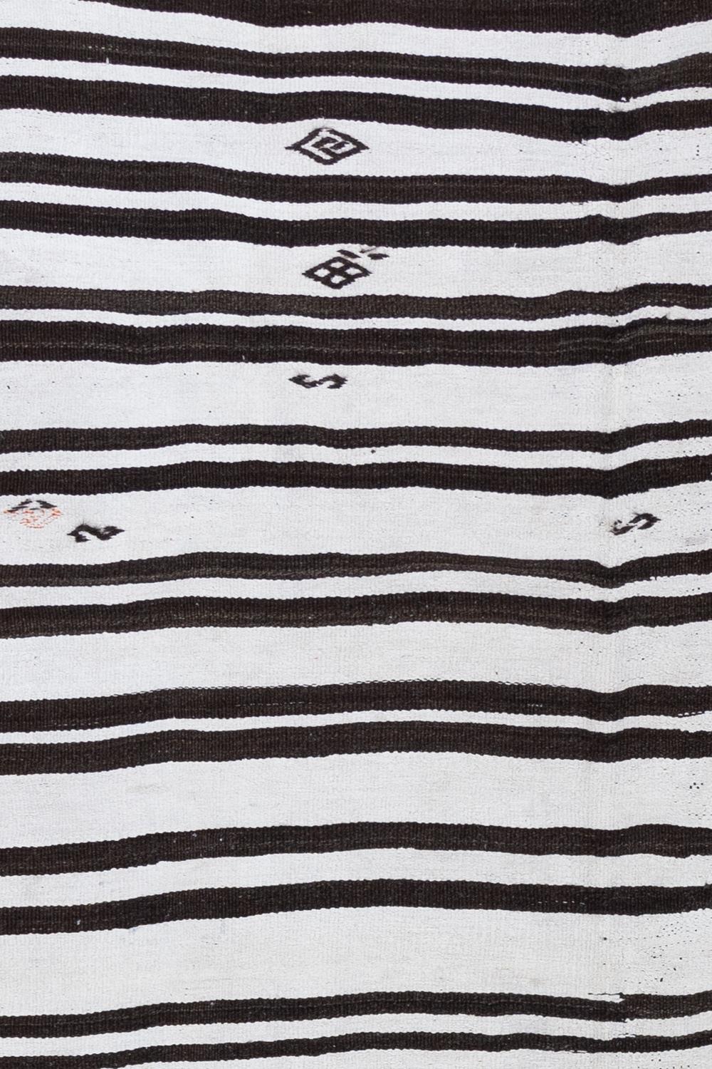 Age: Circa 1950

Colors: Washed black, Espresso, and bone, with a tiny pop of Terracotta. 

Pile: Flatweave

Wear Notes: 2

Material: Hemp, wool. 

Traditional hemp Kilim with contrasting dark stripes. The inclusion of ribbon and evil eye symbols