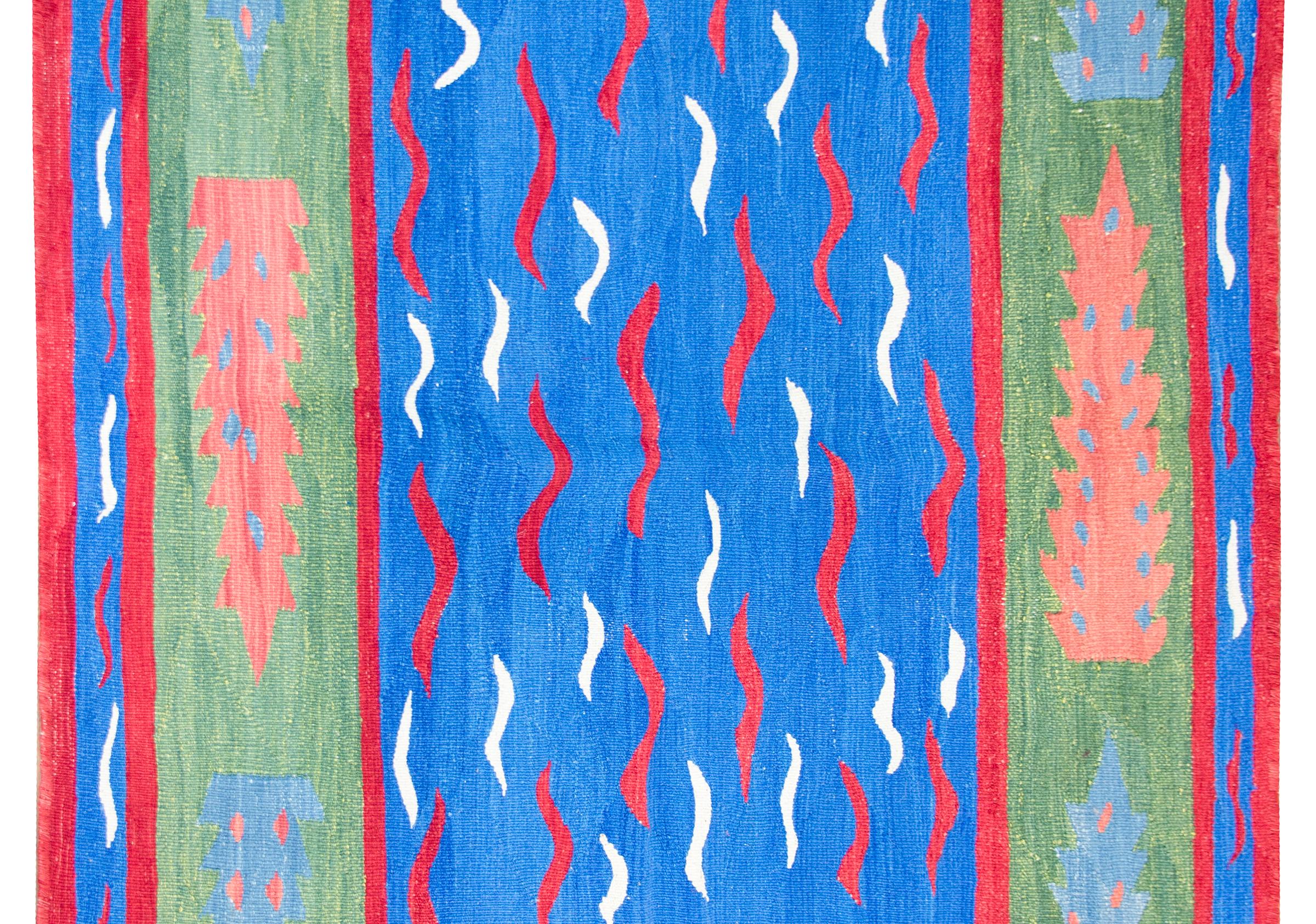 A bold and powerful late 20th century Turkish kilim rug with red and white wavy lines against a bright royal blue ground, surrounded by a green border with stylized cypress tree, and all surrounded by another border with even more red and white wavy