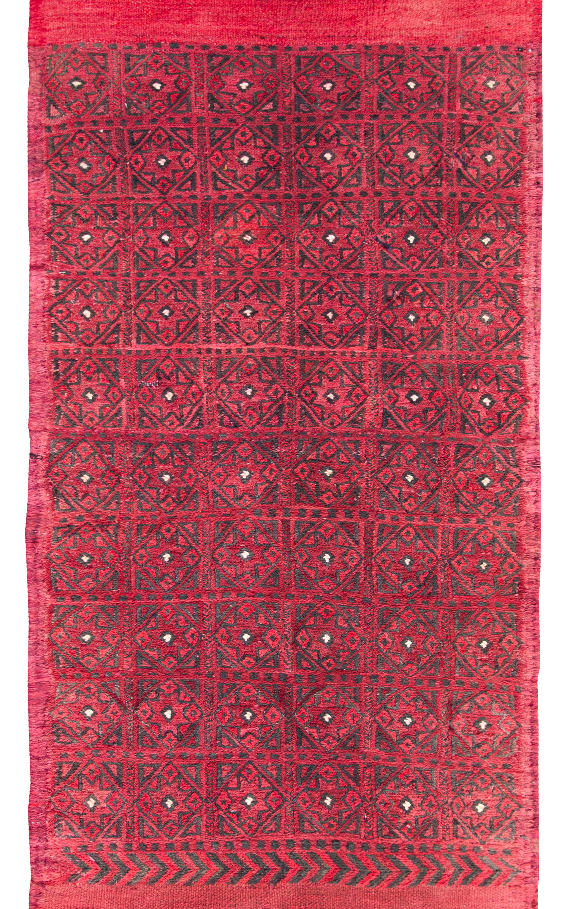 A bold vintage mid-20th century Turkish Kilim runner with a repeated diamond pattern set against a crimson background with an asymmetrical fringe border, one side with a chevron pattern and the other with two black stripes.  