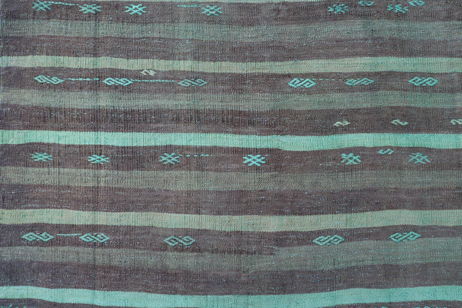 Mesures : 7'1 x 10'2 Ce tapis kilim turc vintage présente un mélange harmonieux de tons terreux et de turquoise vibrant. Le fond est constitué de bandes alternées de brun foncé et de brun clair, créant ainsi une base chaleureuse et accueillante. Des