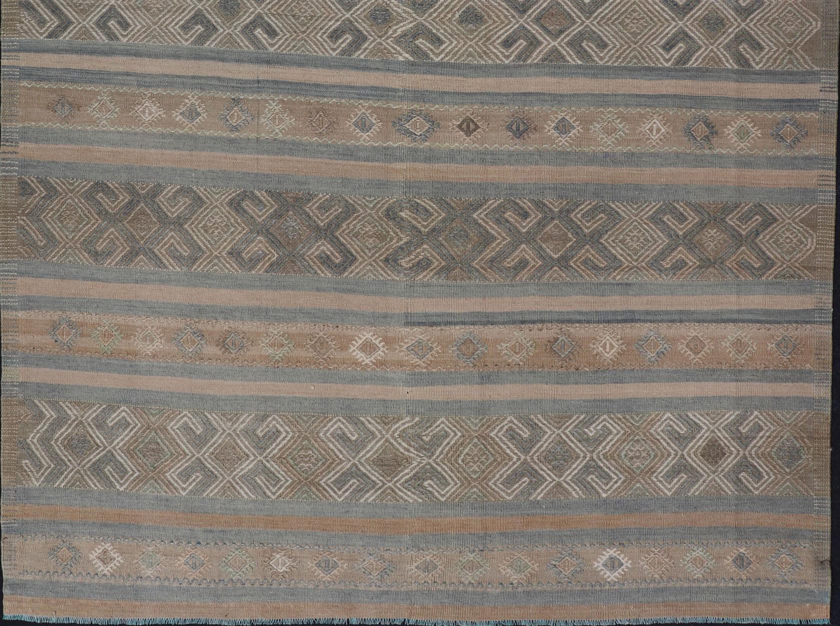 This flat-woven Kilim from Turkey features an enticing composition consisting of stripes with fascinating geometric designs rendered in natural tones of brown and tan, taupe, as well as some blue shades. 

Measures: 5'7 x 8'8.

Vintage Turkish