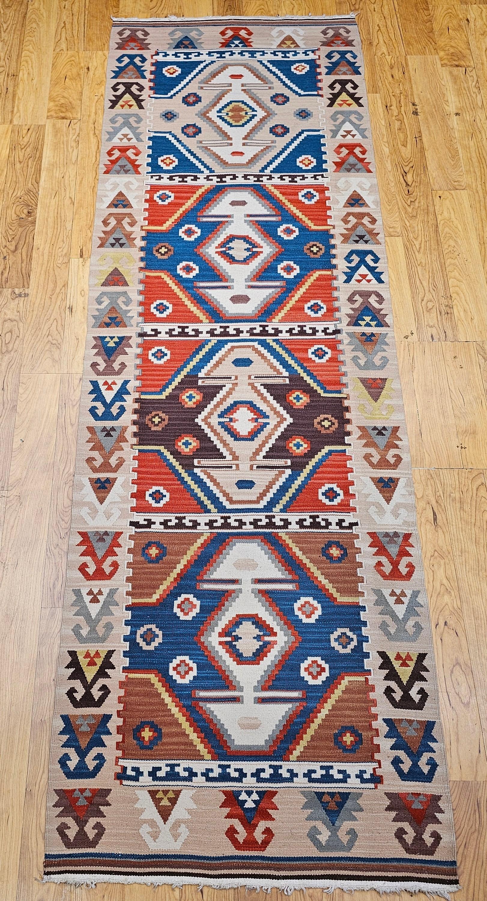Ce chemin de table Kilim turc vintage, tissé dans le 3e quart du 20e siècle, présente un motif géométrique saisissant avec quatre médaillons axiaux proéminents. Réalisé dans une palette audacieuse mais terreuse de bleu, rouge, marron et ivoire, le