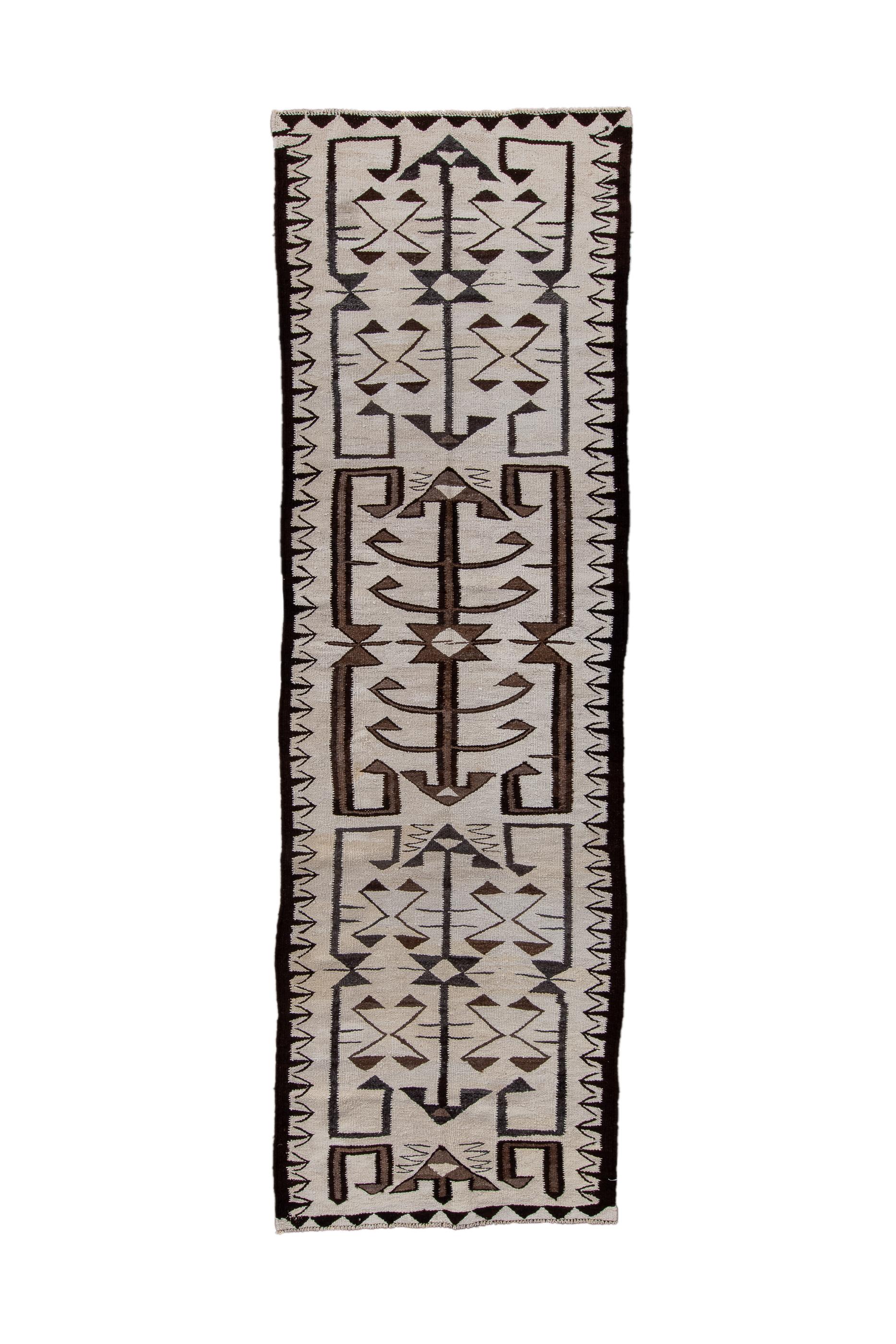 The ecru beige field of this tapestry woven pileless runner shows a pattern akin to that of Turkmen tent bands, also on light grounds. There is a tripartite layout with central poles bracketed by four straight and end curled shapes. The central