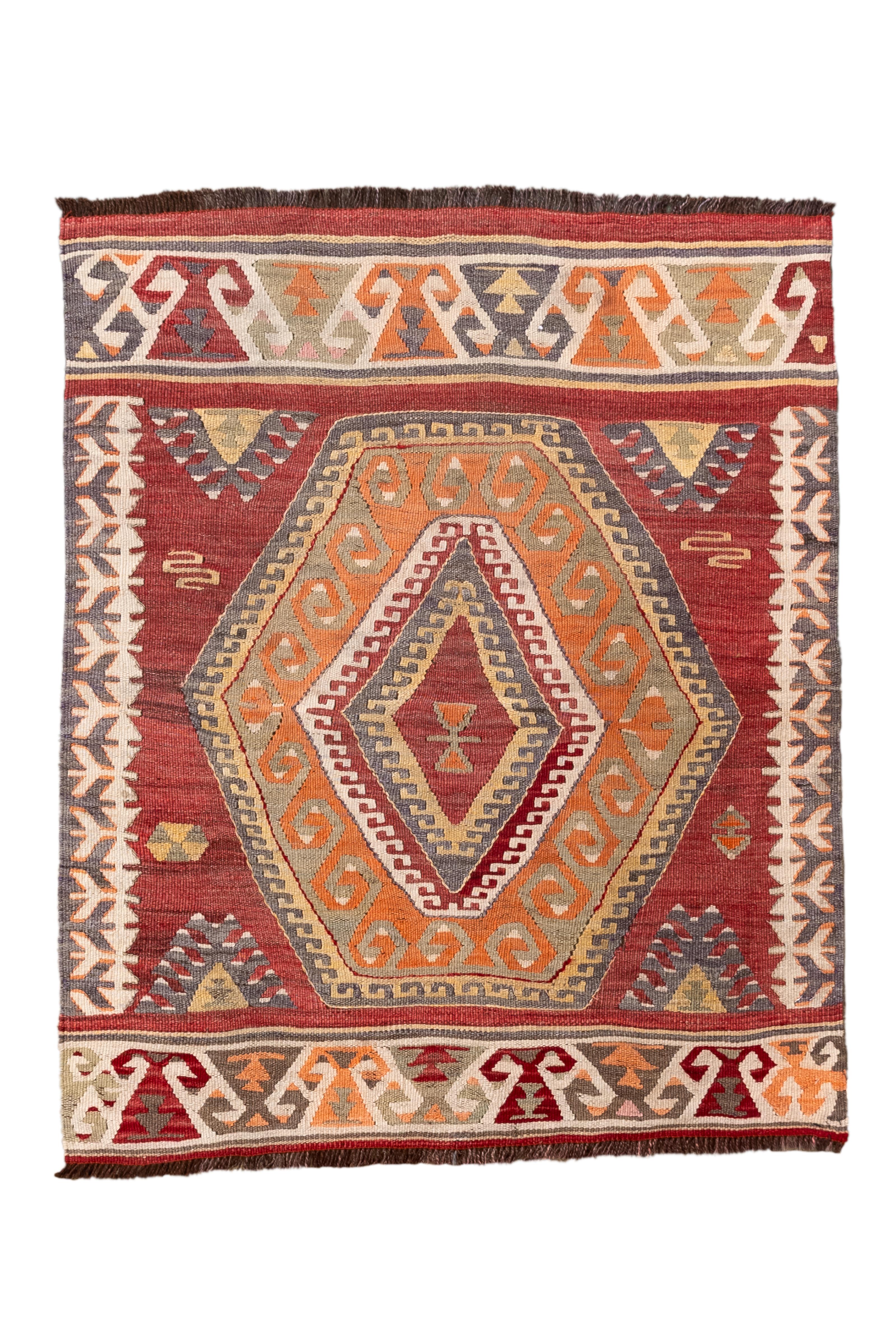 Questo vivace tappeto Kilim turco vintage presenta un imponente medaglione esagonale centrale, annidato all'interno di una sorprendente composizione geometrica. Il campo rosso mattone intenso fa da sfondo ai toni dell'arancio bruciato, dell'ocra,