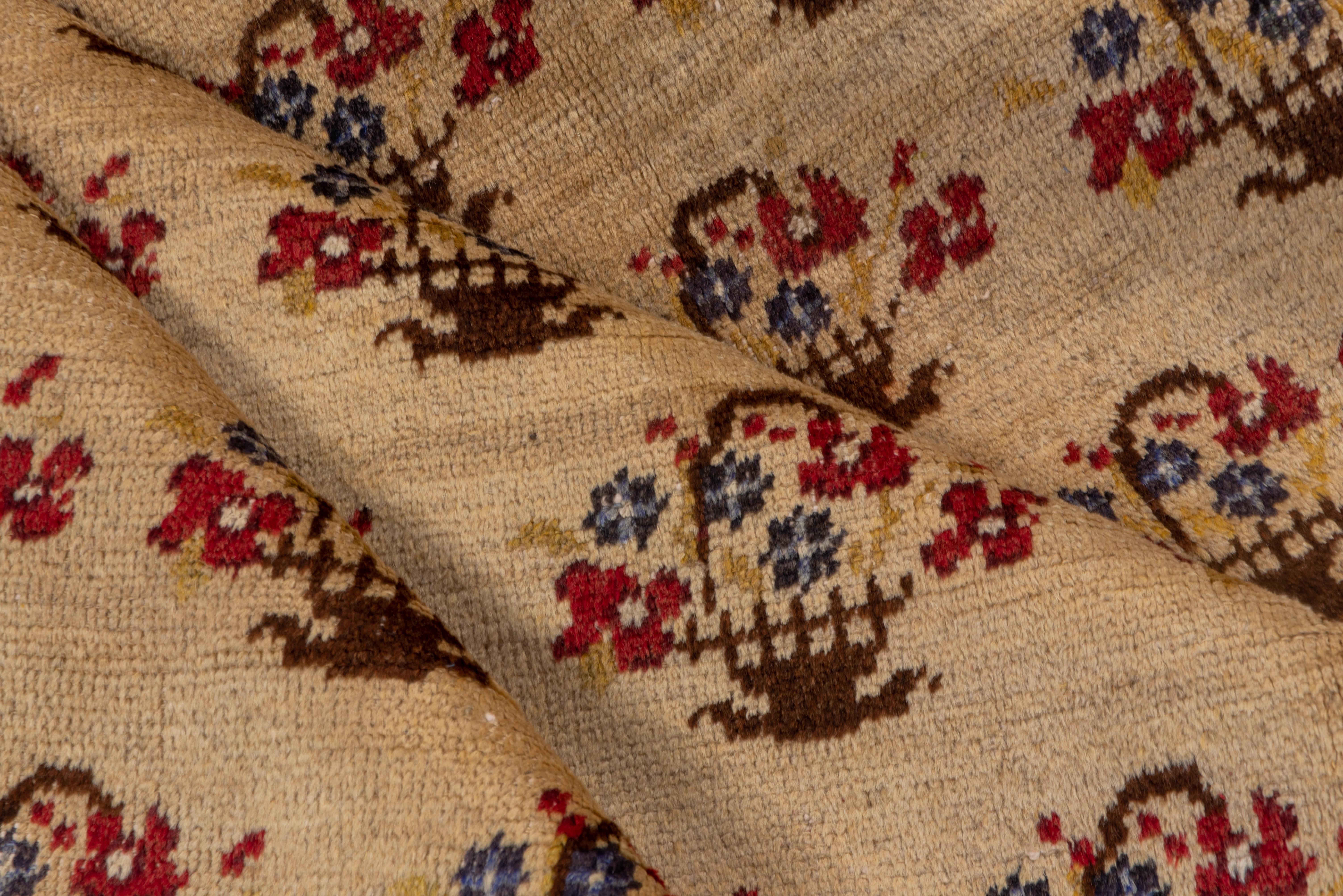 This essentially borderless central Anatolian village rug shows 22 offset rows of basket and flower motives accented in red and blue on a warm cream ground. The pattern clearly derives from a textile sources. Homey. Good condition.
  