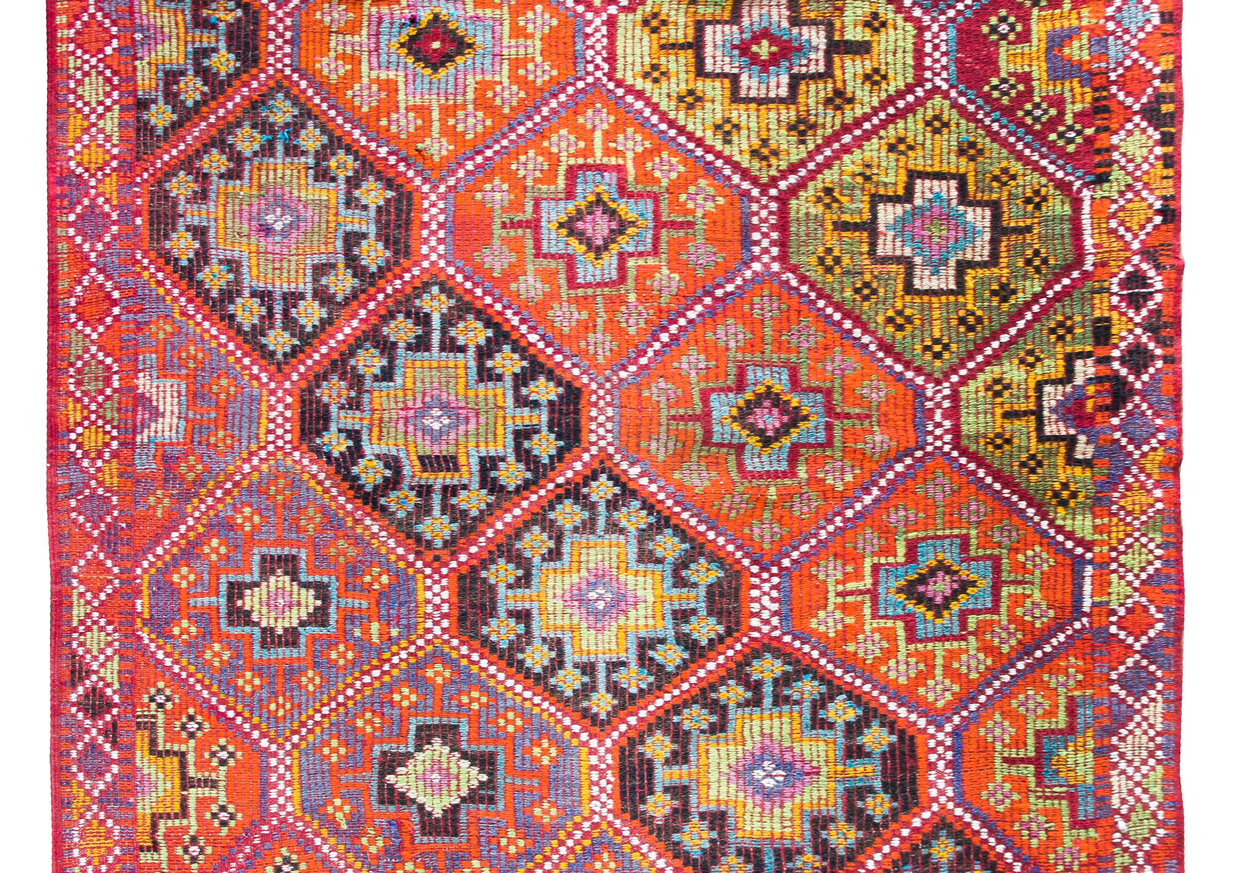 Chic et audacieux, ce tapis turc de Konya du milieu du XXe siècle présente un magnifique motif de médaillons en losange avec des fleurs stylisées organisées en bandes diagonales et tissées dans des tons orange, or, indigos clairs et foncés, blancs,