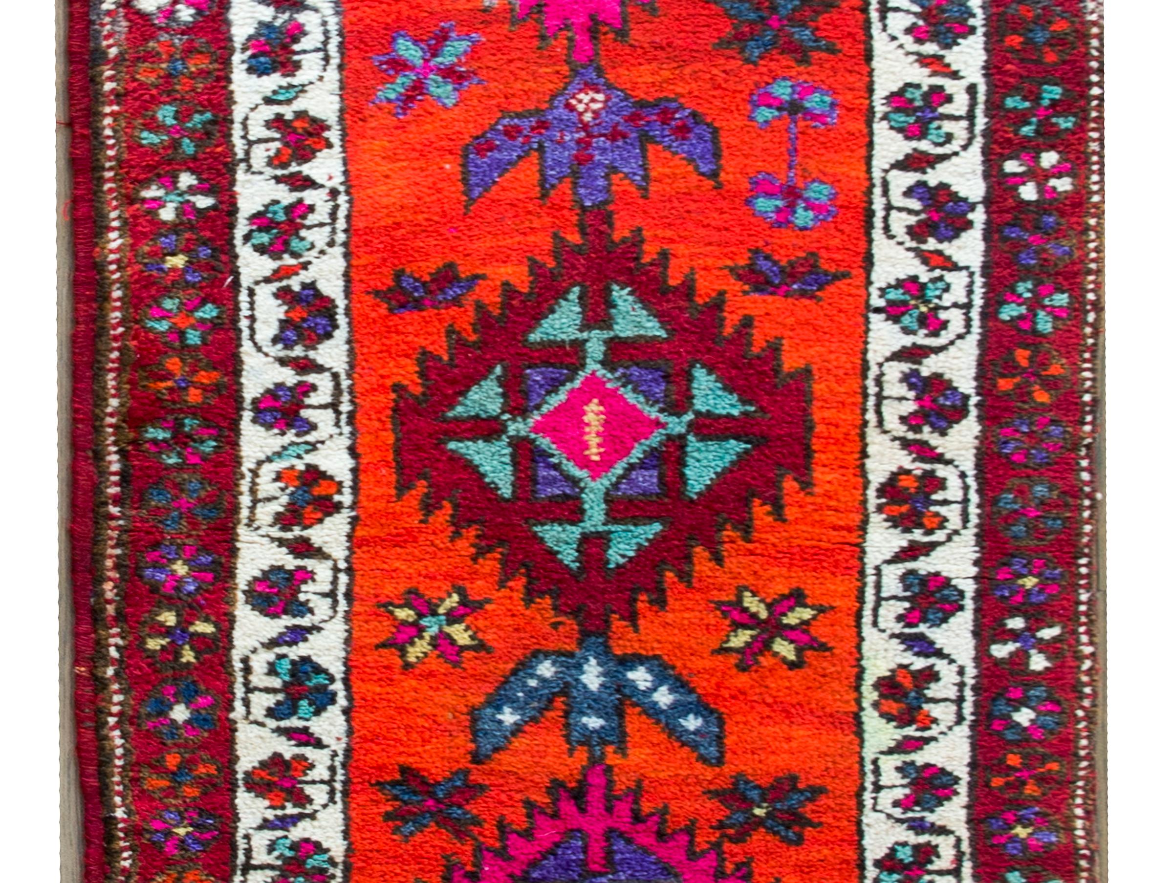 A brilliant late 20th century Turkish Konya runner with seven large brightly colored stylized flowers amidst a field of more flowers, and set against an abrash orange background. The border is simple with two different floral and scrolling vines