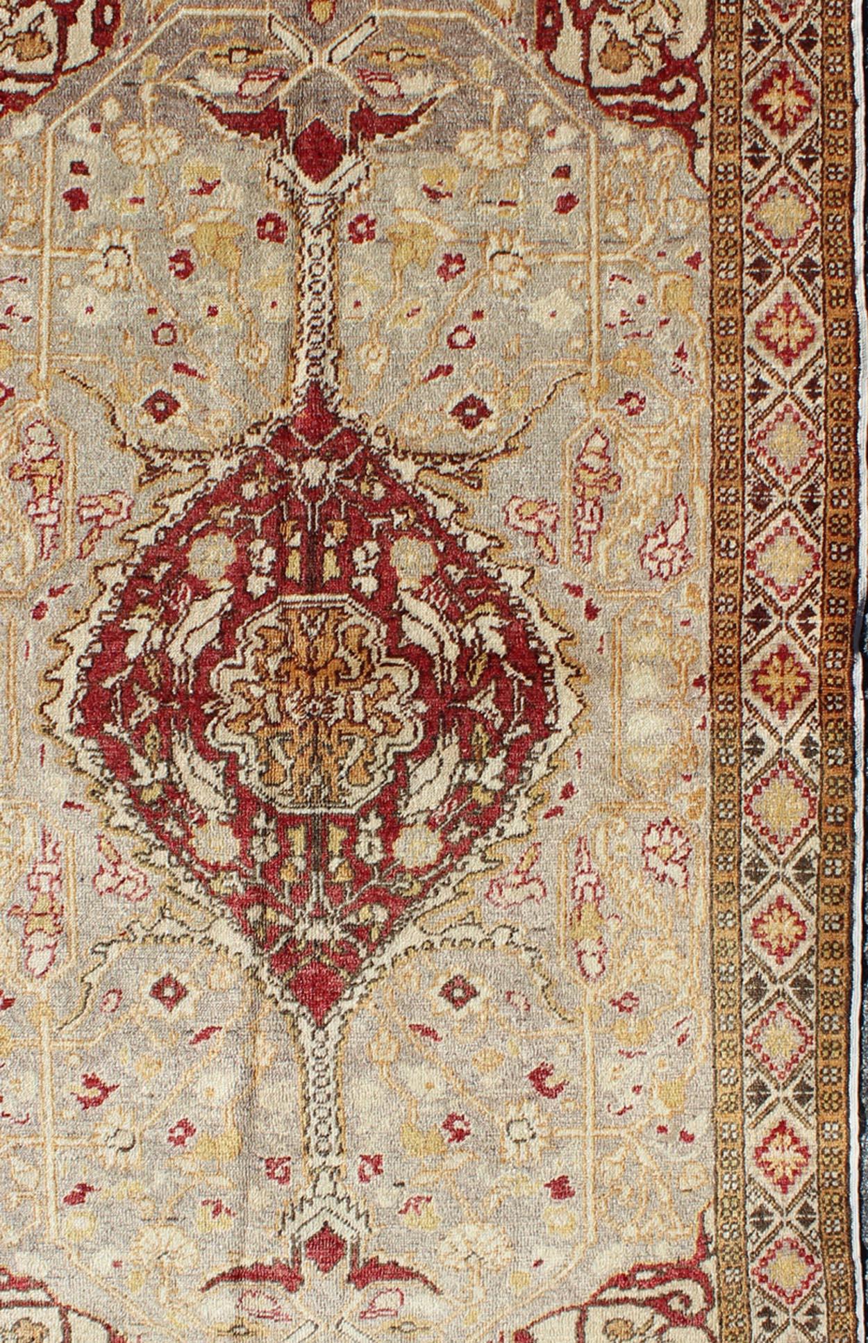 Measures: 4 x 6'8

This vintage Turkish Oushak carpet (circa mid-20th century) features a central medallion design, as well as patterns of smaller floral shapes and botanical elements in the four cornices, and geometric diamonds in the borders.