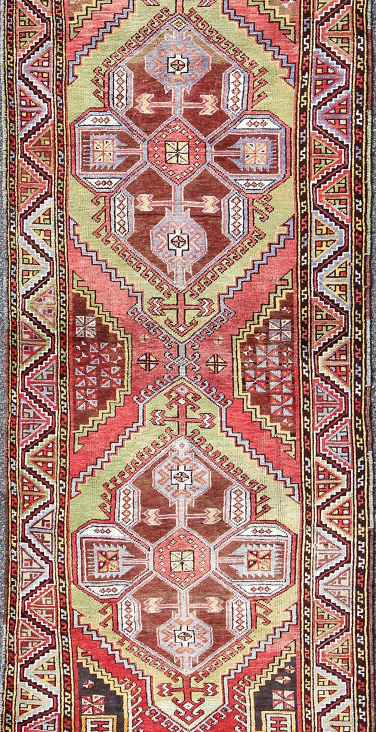 Measures: 3'7 x 10'10

This vintage (circa 1940's) Turkish Oushak runner features bright, vibrant spring colors, such as rose red, grassy green, lavender, blue, and pink. The border hails a tribal zig-zag design, while the field displays large,
