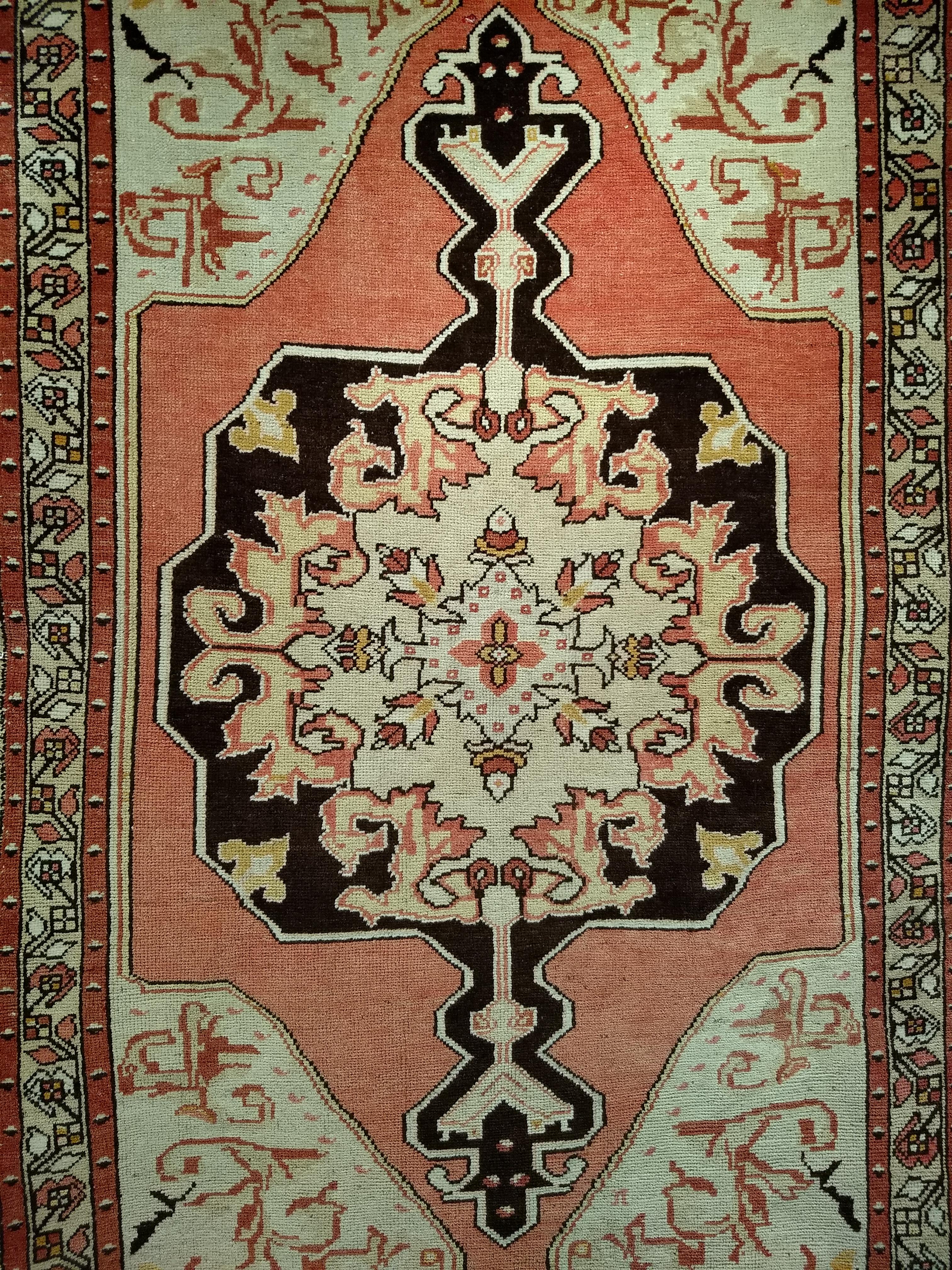 A beautiful Turkish Oushak rug from the early 1900s. The rug has a cream field color and a large central medallion in light red color. The medallion in dark chocolate color is set in a larger medallion in light red color. The combination of mellow