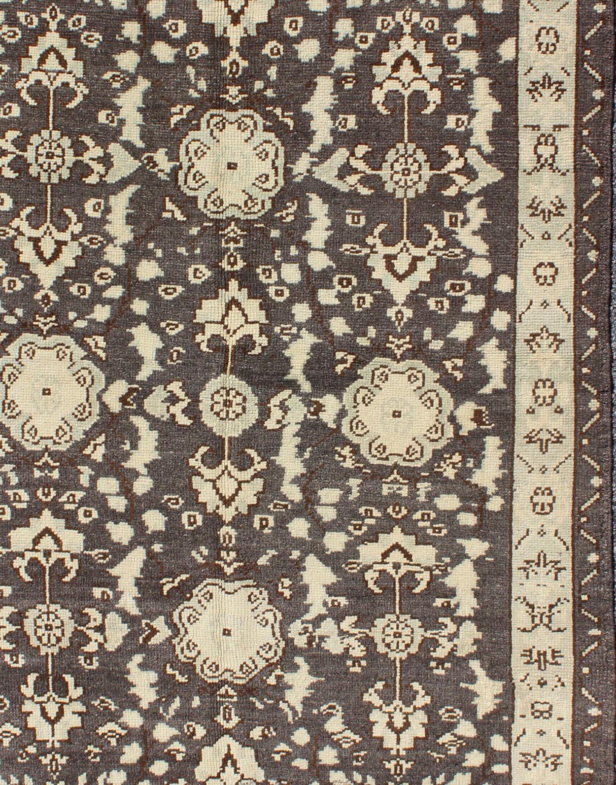 Measures: 3'9 x 5'10.

This vintage Oushak was hand-knotted in Turkey during the 1940's. The charcoal/gray background dark brown highlights field displays clover motifs and other nature designs in antique white with accents in a soft, pale jade.