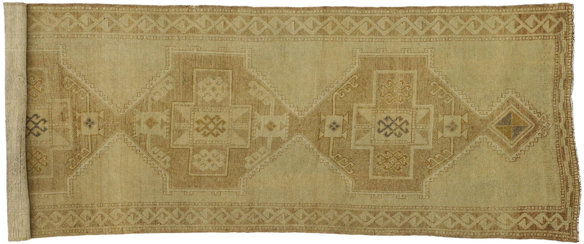 This subtle vintage Turkish Oushak carpet runner bears a remarkable air of chic sophistication with its modern style and muted colors. A beautiful display of elegant medallions delicately weaved as if they are floating in the light brown field. The