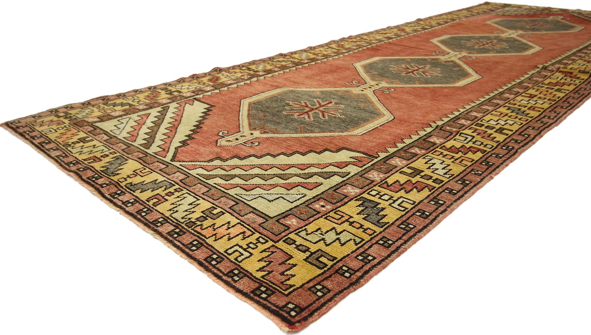 This hand-knotted wool vintage Turkish Oushak runner features a modern tribal style. Immersed in Anatolian history and vibrant colors, this vintage Oushak rug runner is combined simplicity with sophistication. The abrashed field showcases a row of