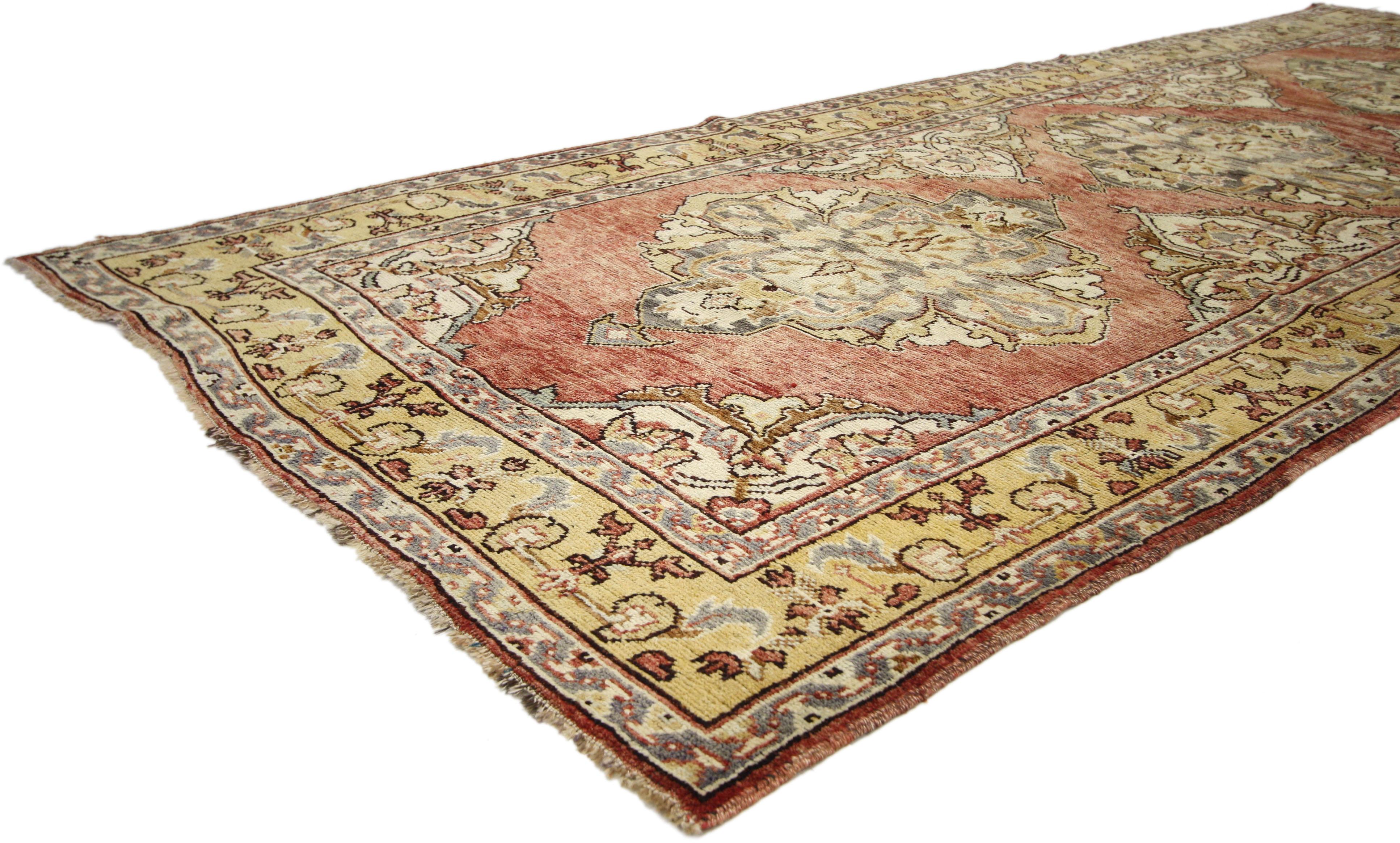 73987, tapis turc vintage Oushak Gallery, large couloir. Chaleureux et accueillant, ce tapis galerie Oushak turc vintage en laine nouée à la main présente trois médaillons ornés dans un champ rouge abrash avec un motif floral sur toute la surface.